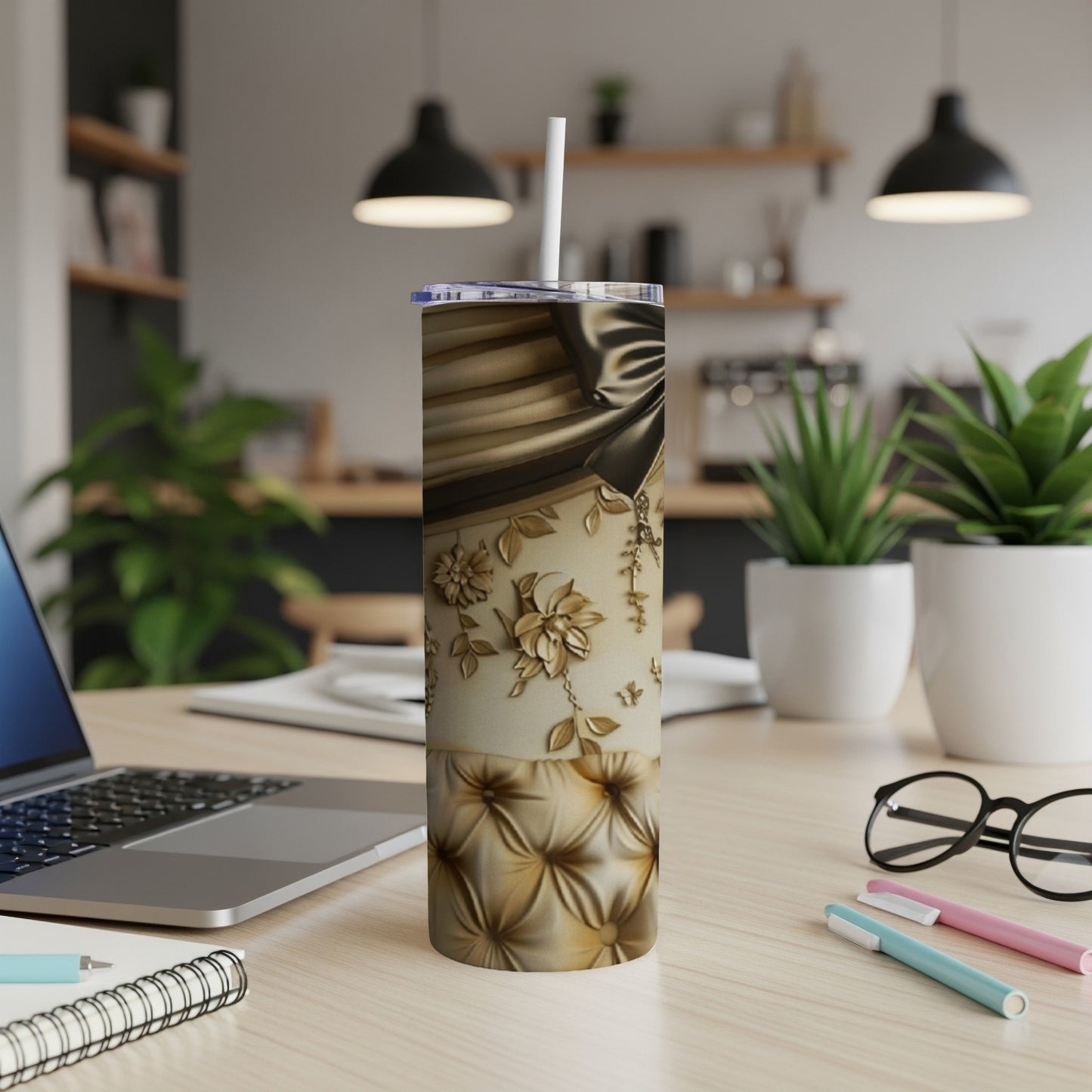 Gold and cream patterned tumbler with ribbon and floral details on a desk.
