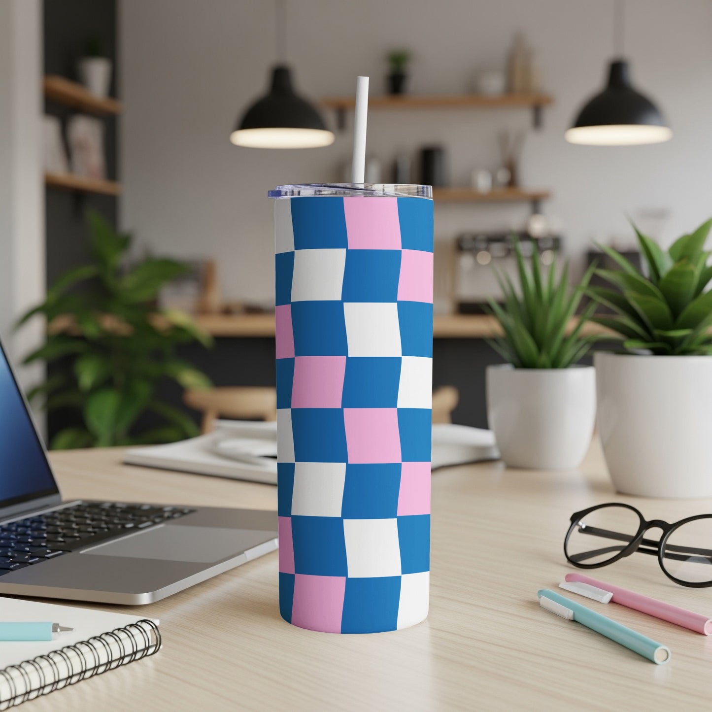 Blue, pink, and white checkered tumbler with straw on desk.