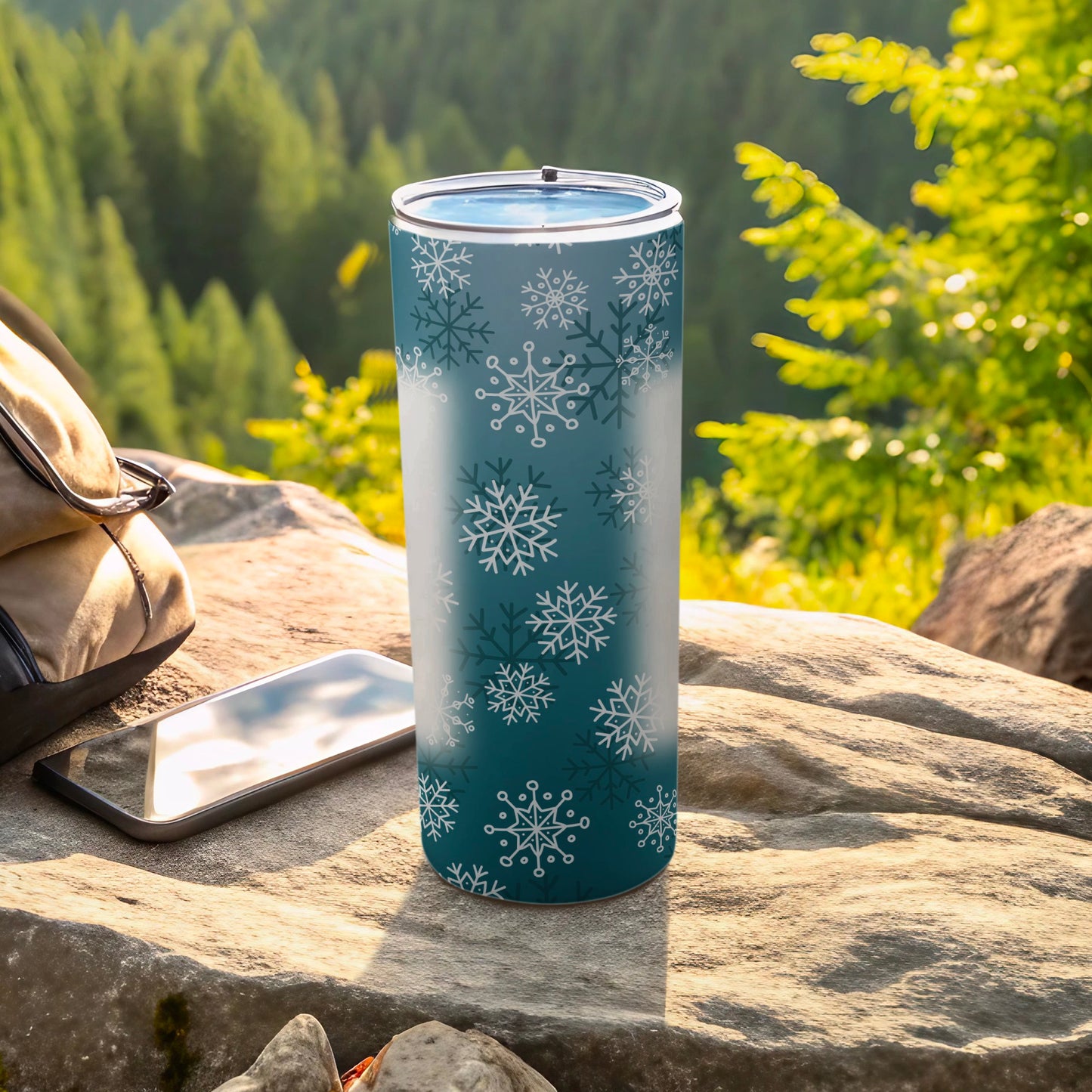 Teal tumbler with white snowflakes, next to phone and backpack.
