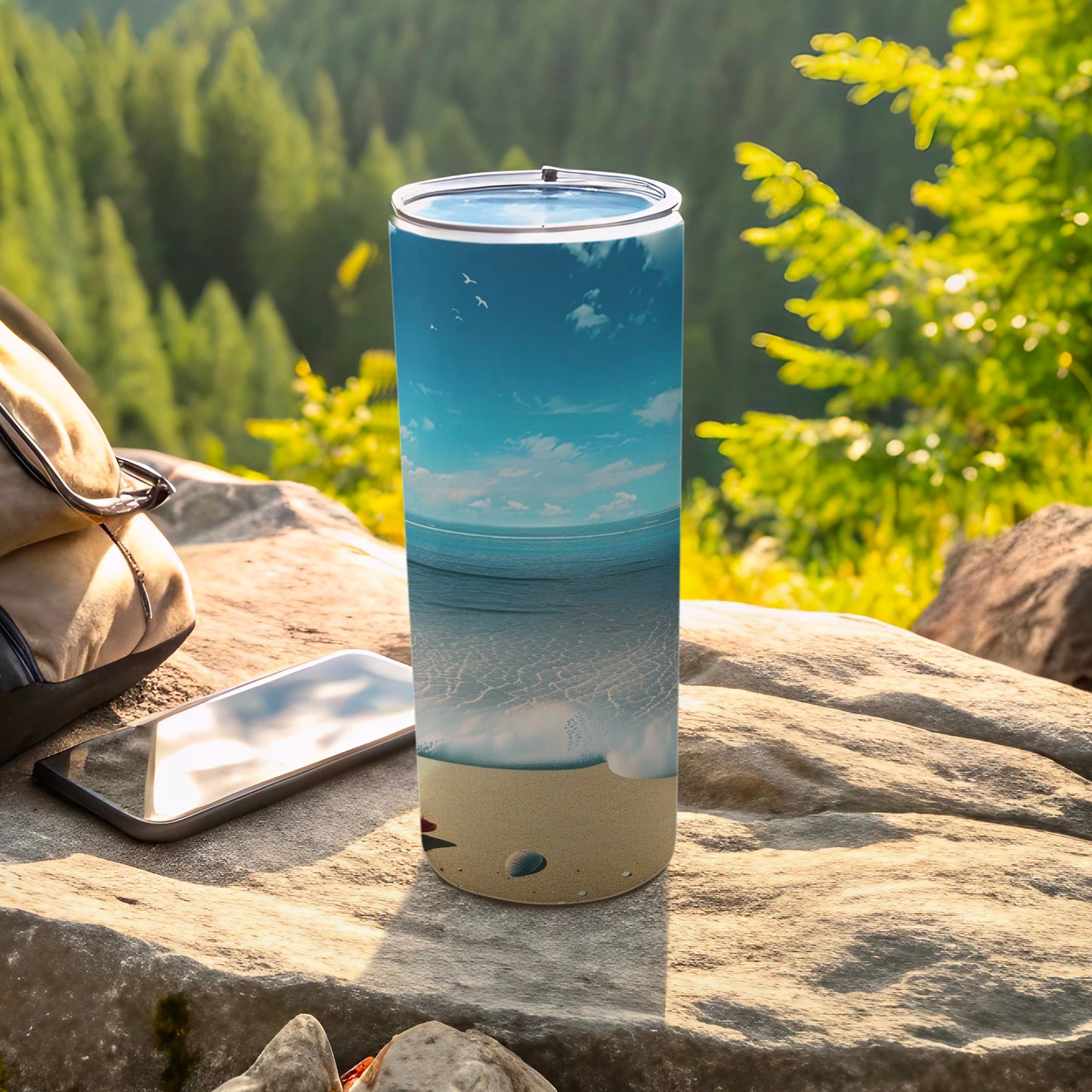 Tall tumbler with beach and ocean scene, resting on rock with phone.