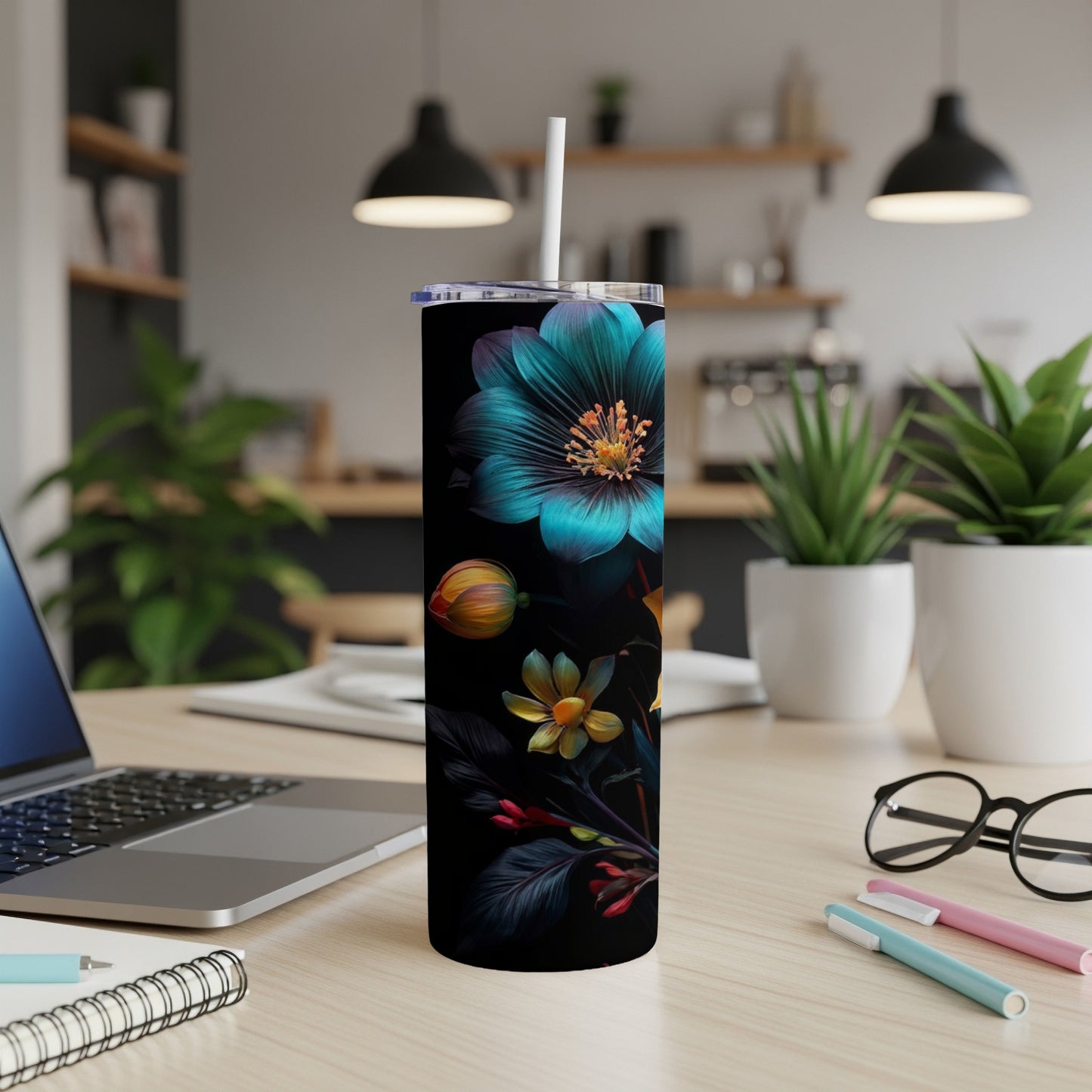 Teal floral pattern on black insulated tumbler with straw on a desk.