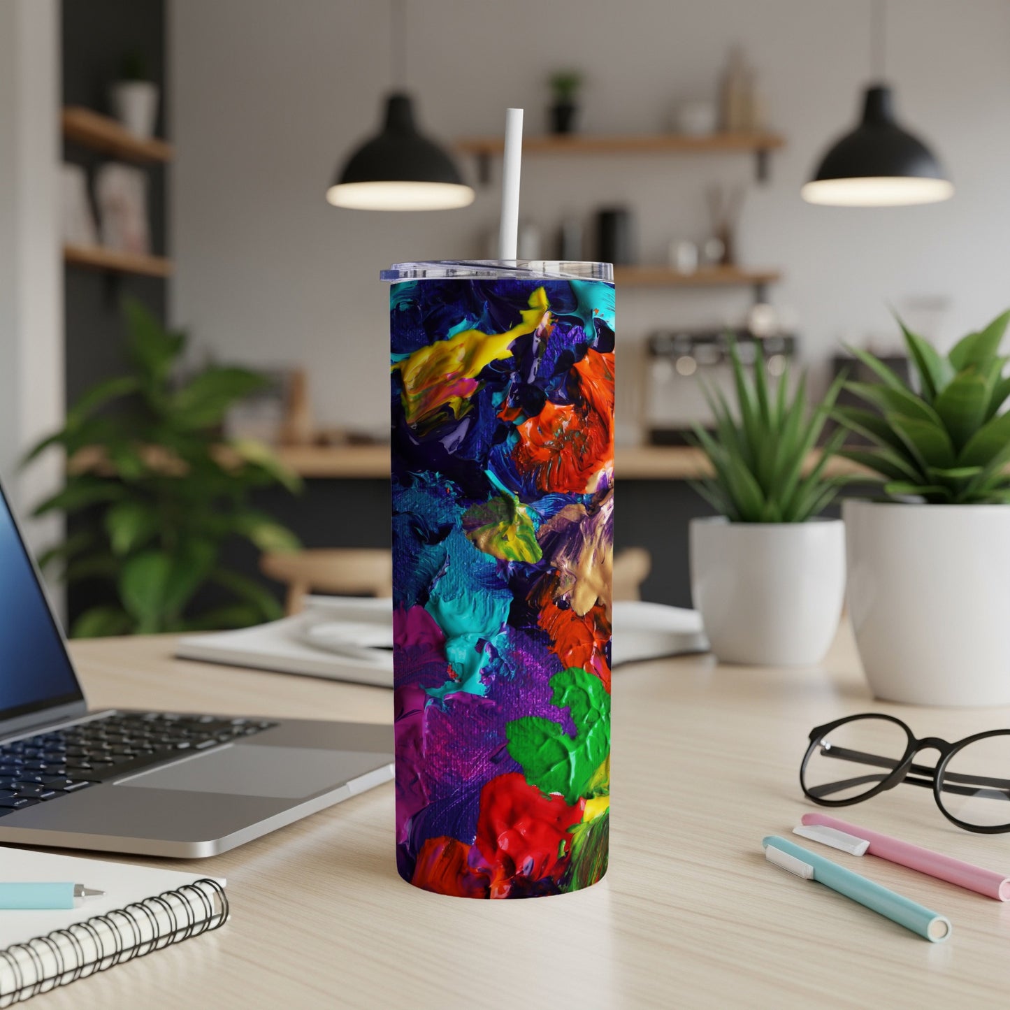 Tall tumbler with colorful abstract paint strokes, straw, on desk.