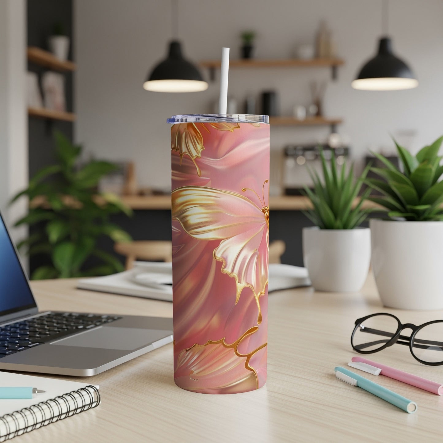 Pink and gold butterfly tumbler on a desk with a laptop and pens.