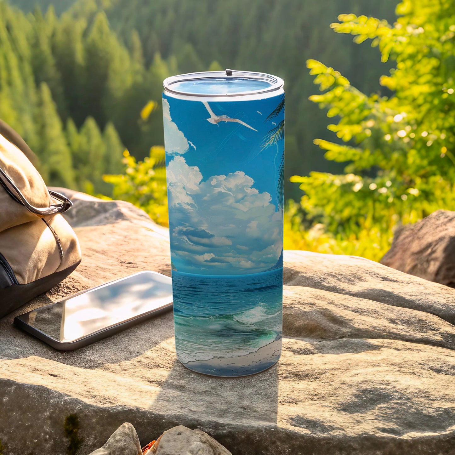 Tall tumbler with a beach scene design, resting on rocks next to a phone and backpack.