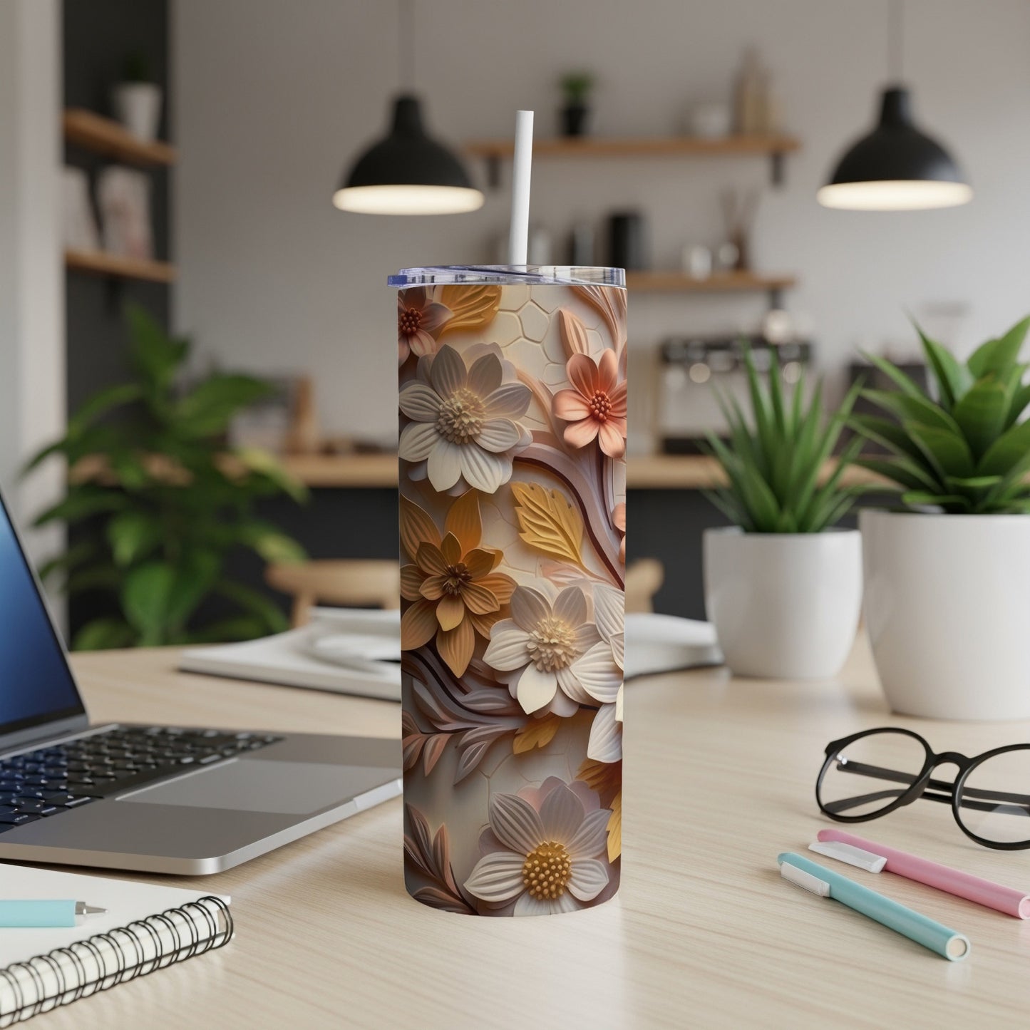 Floral patterned tumbler with straw on a desk with laptop and pens.