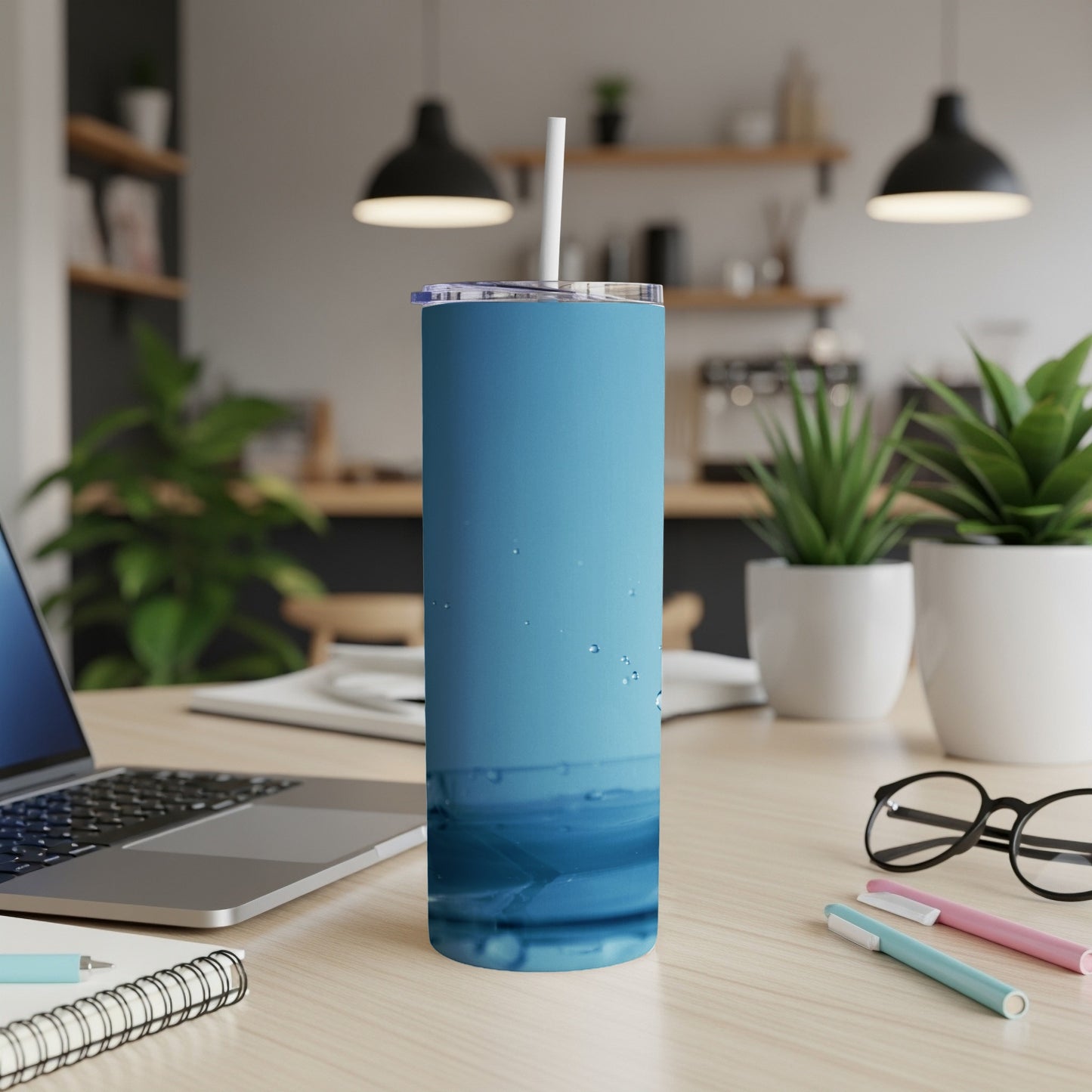 Blue stainless steel tumbler with straw on a desk next to a laptop.