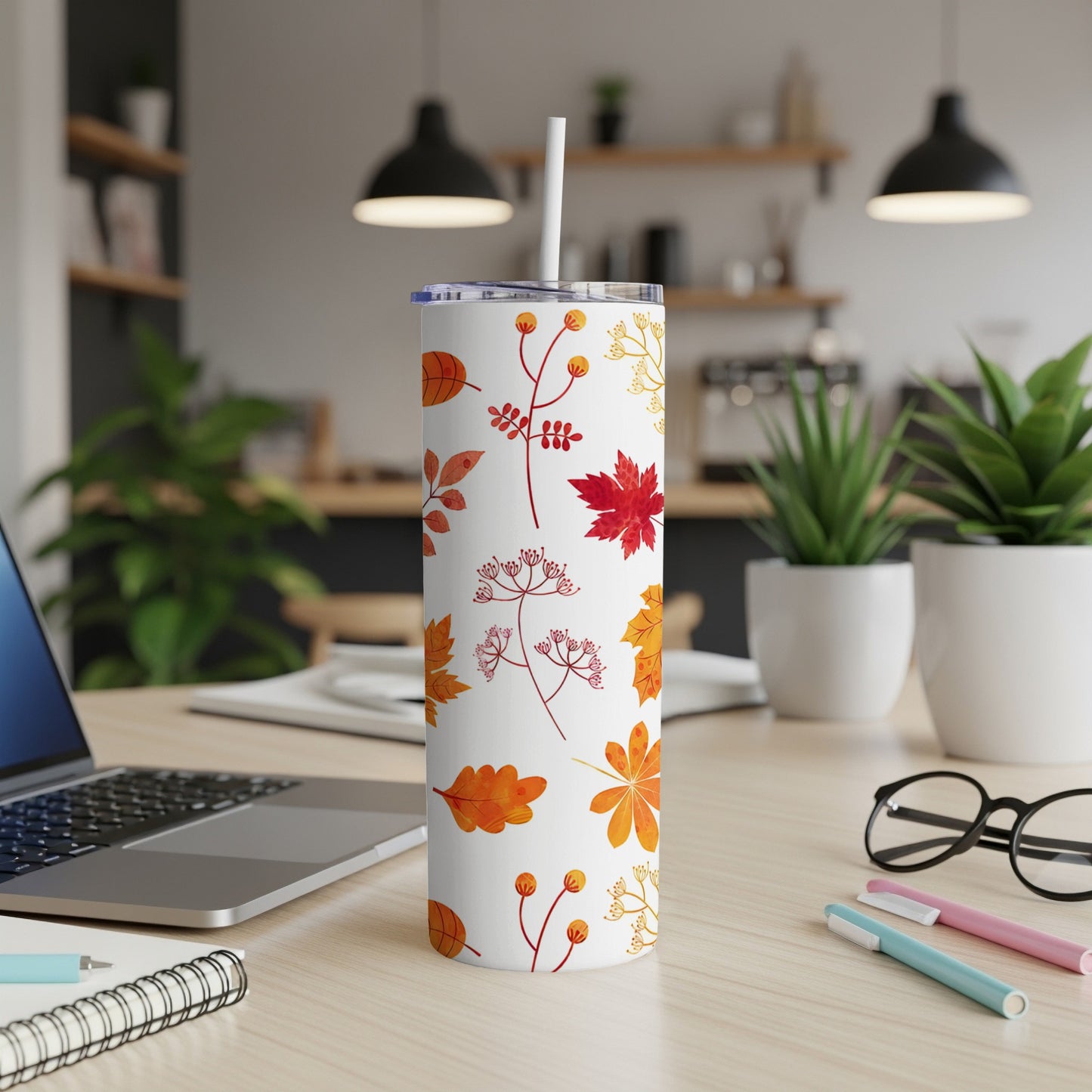 White tumbler with autumn leaf and berry pattern, straw, on a desk.