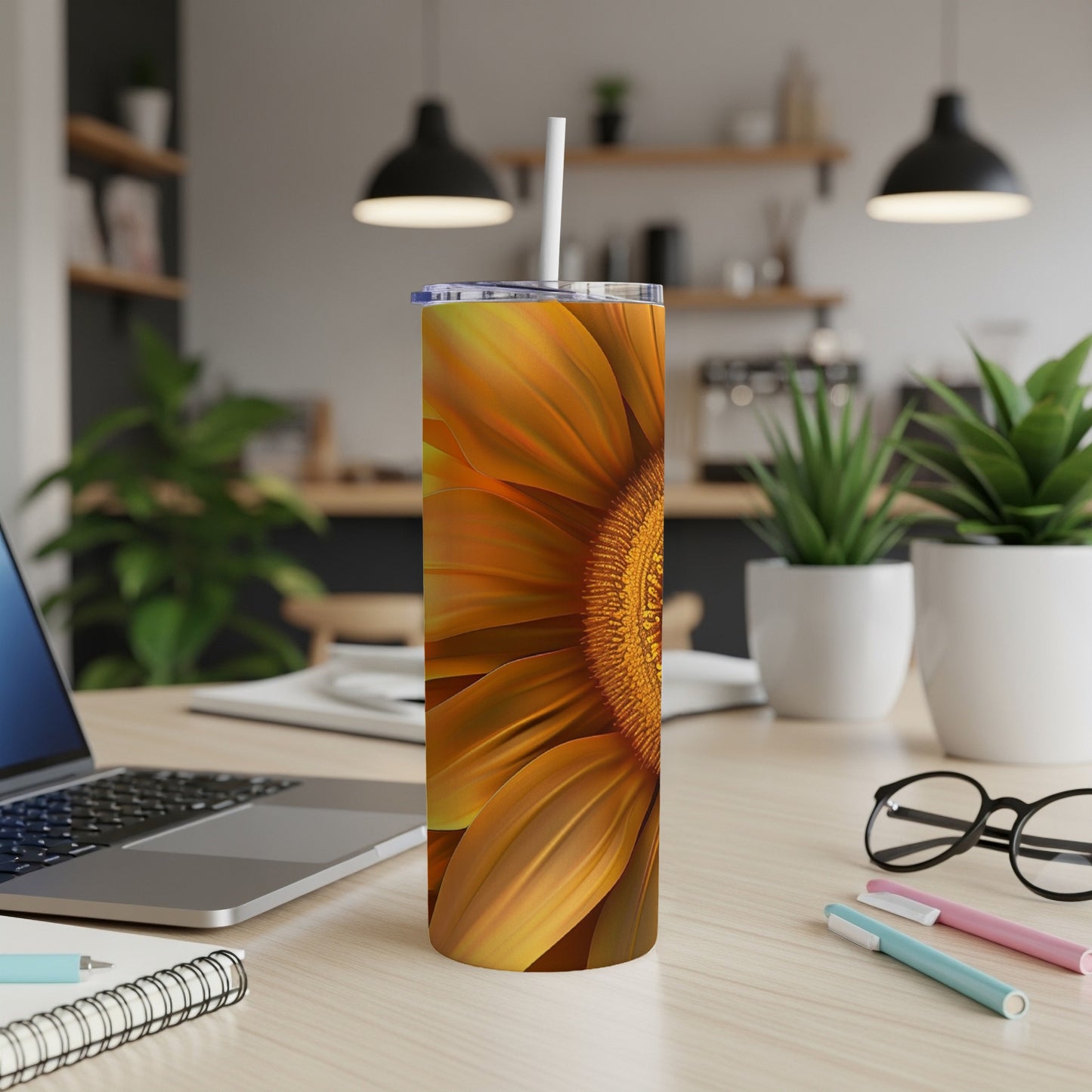 Sunflower tumbler on desk with laptop and pens.