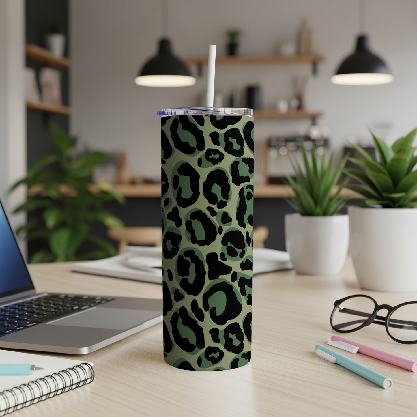 Green leopard print tumbler with straw on a desk with laptop and plants.