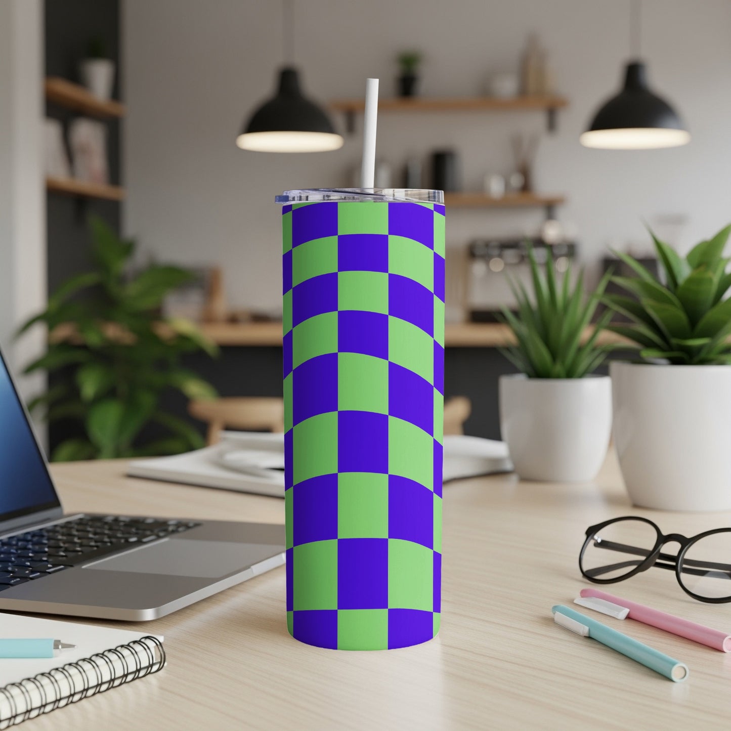 Green and purple checkered tumbler with a straw on a desk.