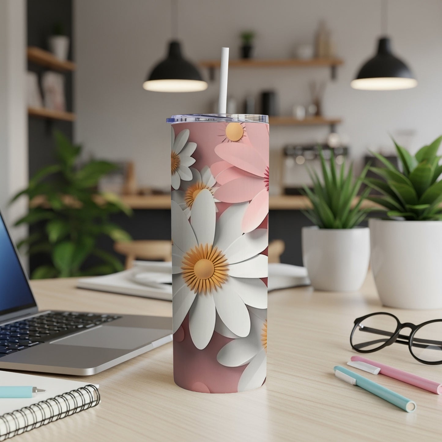 Pink tumbler with white and yellow daisy pattern on a desk.