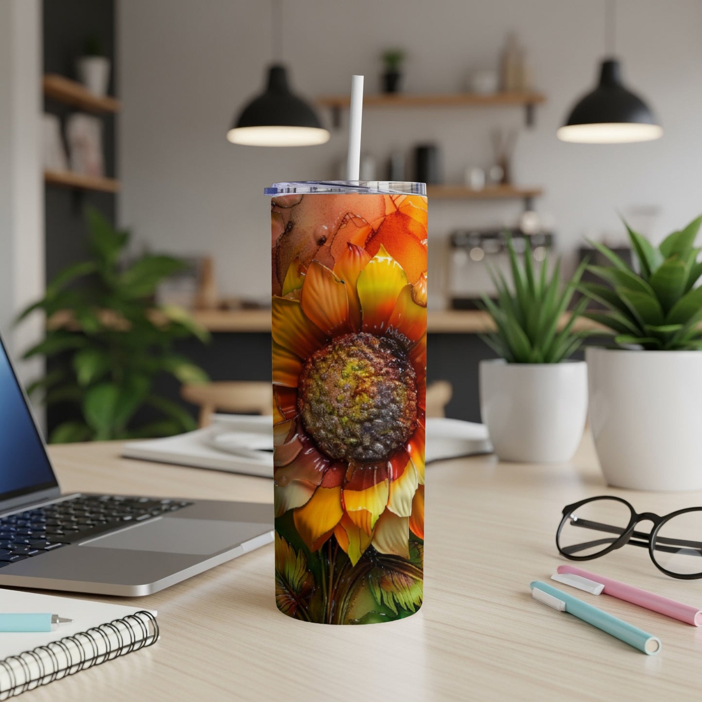 Sunflower tumbler with straw on a desk with laptop and pens.