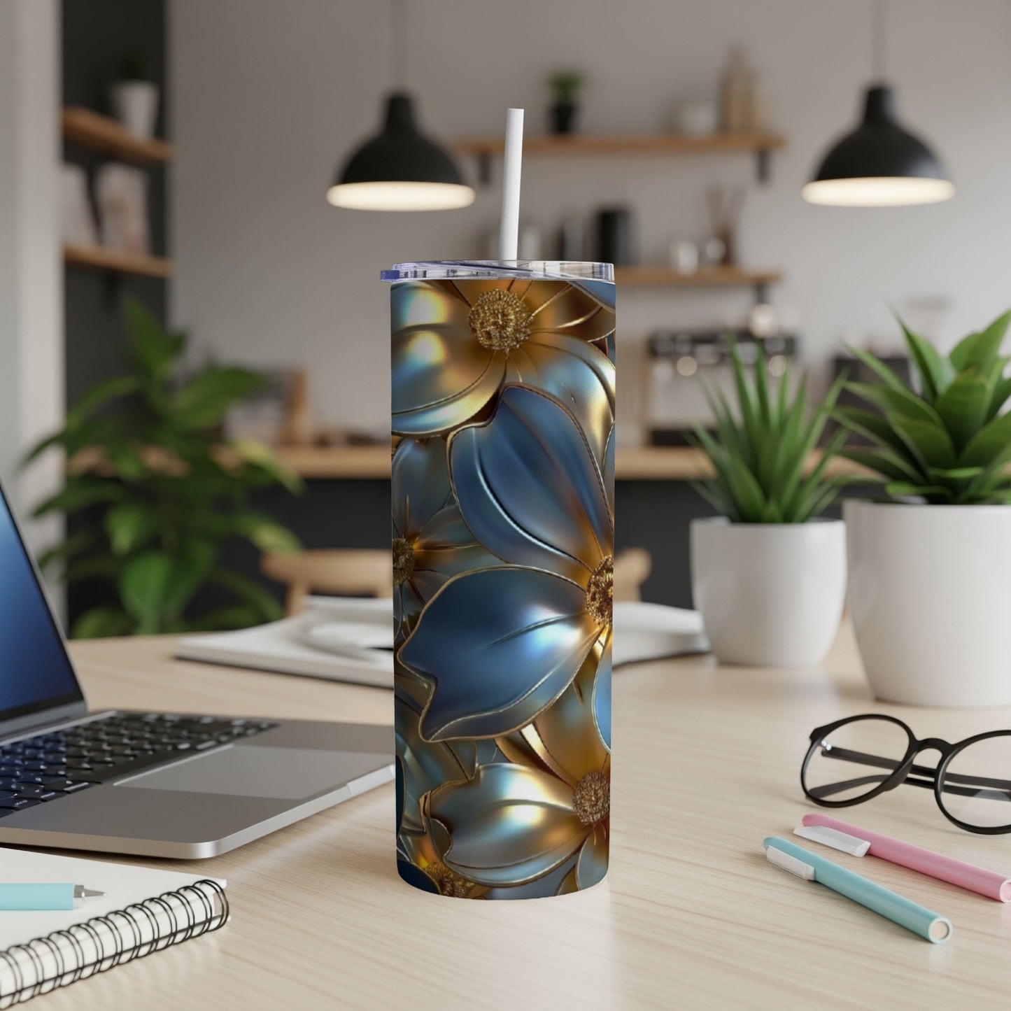 Blue and gold floral pattern skinny tumbler with straw on a desk.