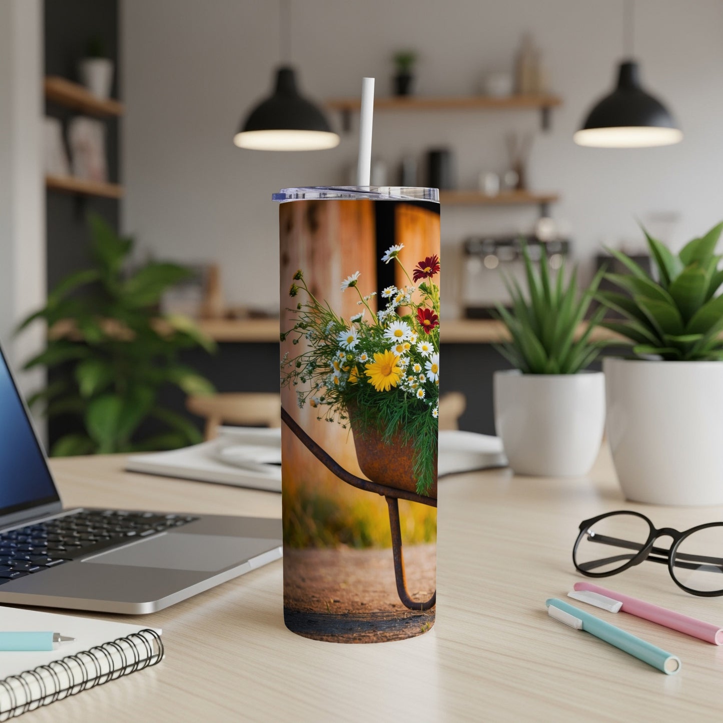Tumbler with colorful flowers in a rustic wheelbarrow on a desk.