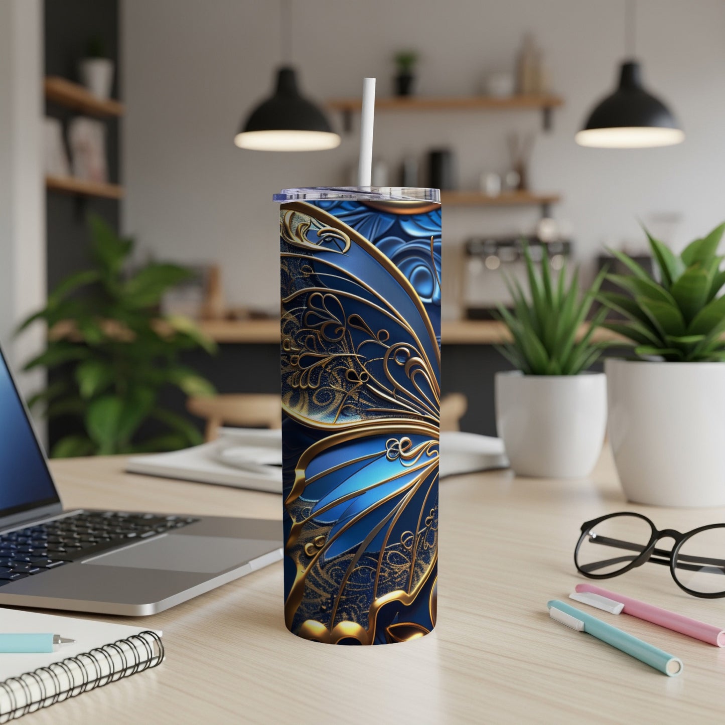 Blue and gold butterfly patterned tumbler with straw on desk.