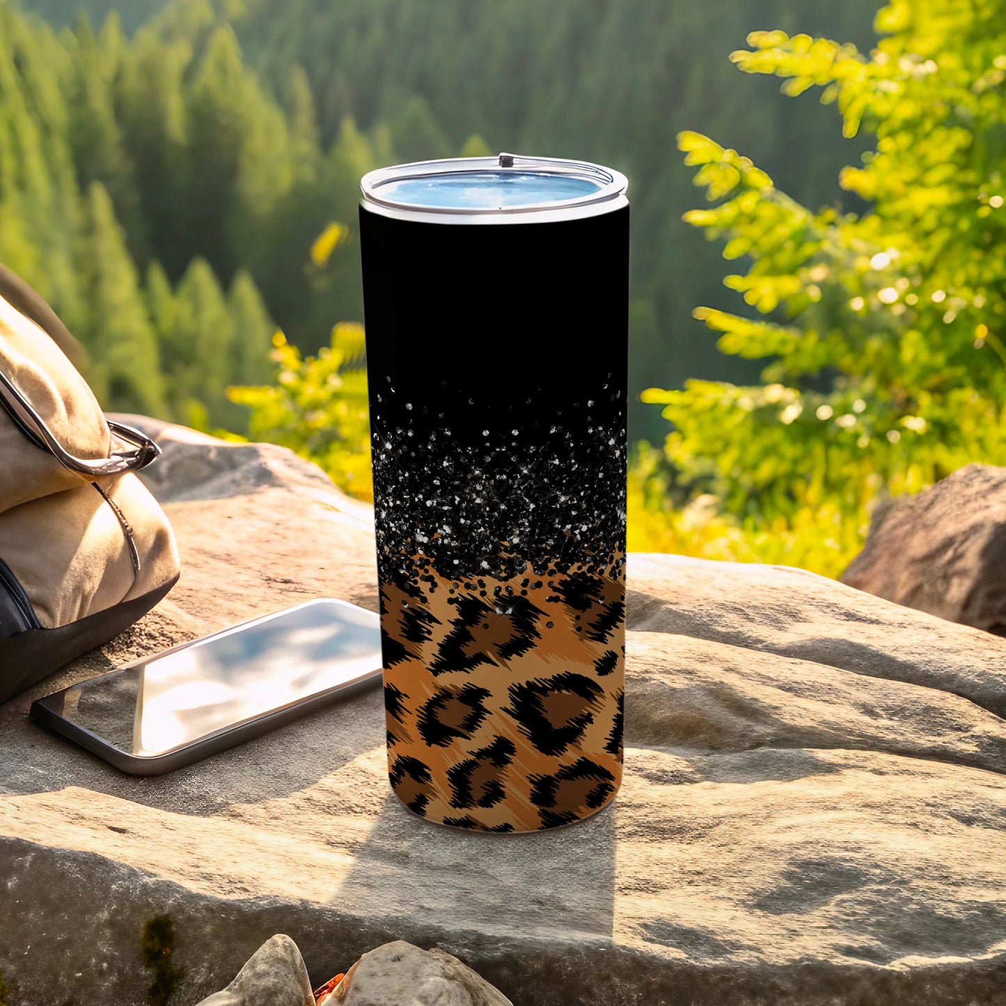 Black tumbler with leopard print and glitter, beside a backpack and phone.