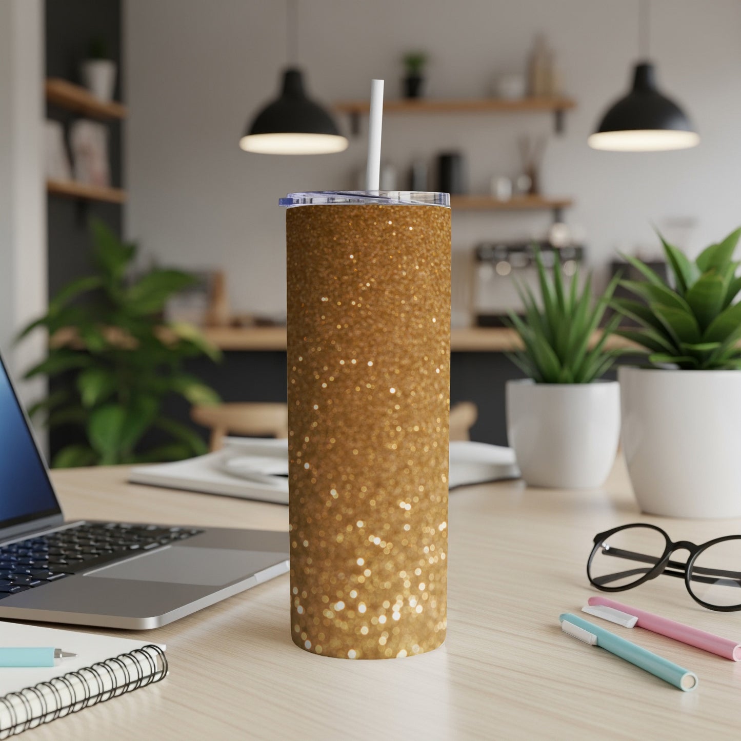 Gold glitter tumbler with straw on desk next to laptop.