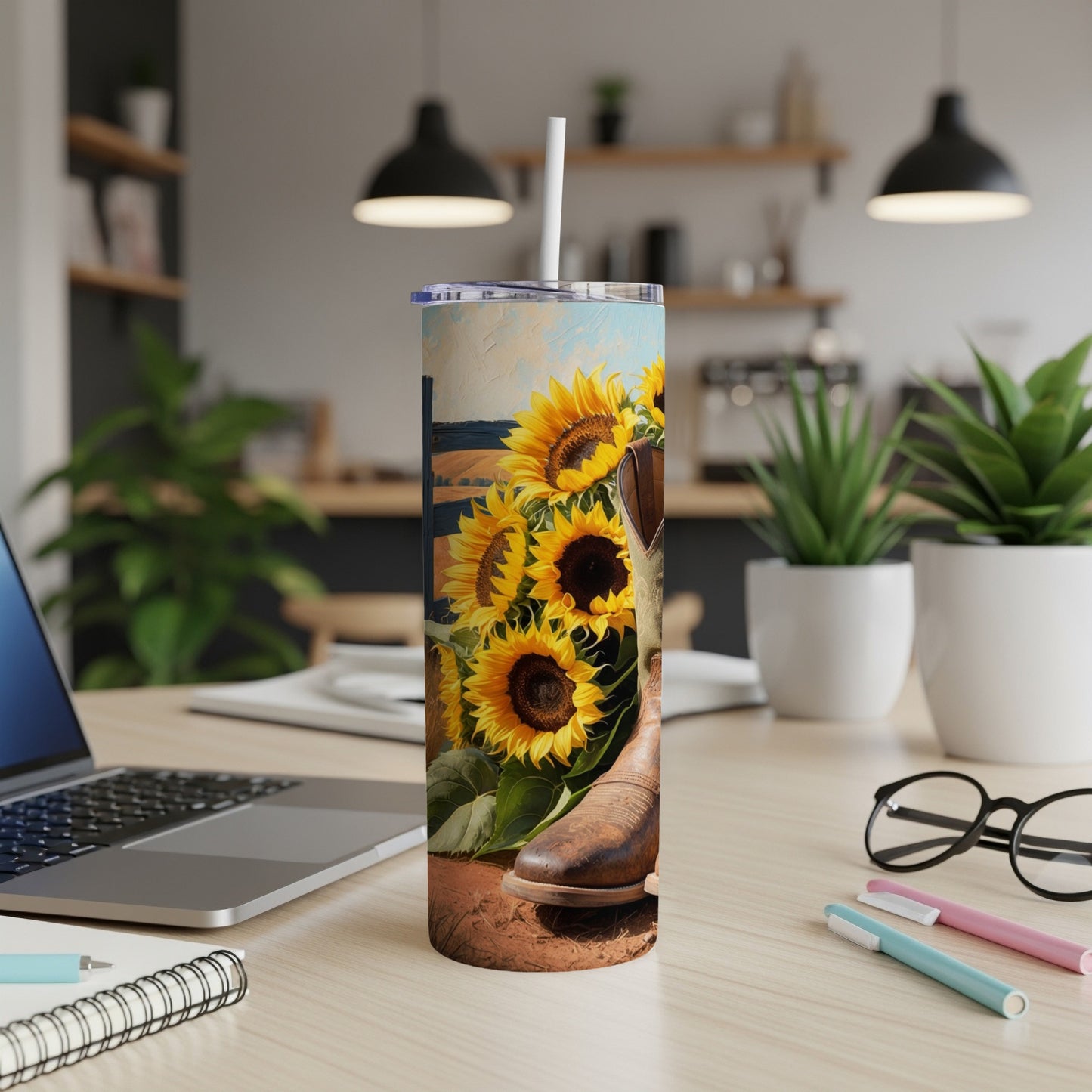Cowboy boot and sunflowers on a tumbler, with a laptop in background.