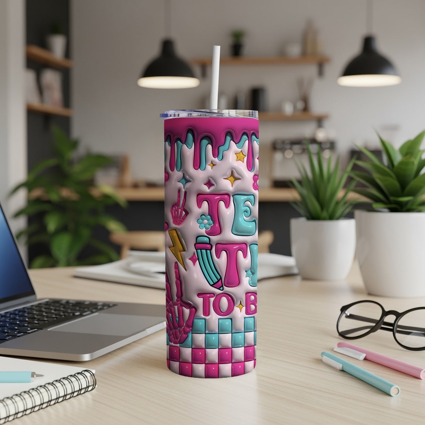 Pink and teal "TEACH TO BE" text on a checkered tumbler with a straw.