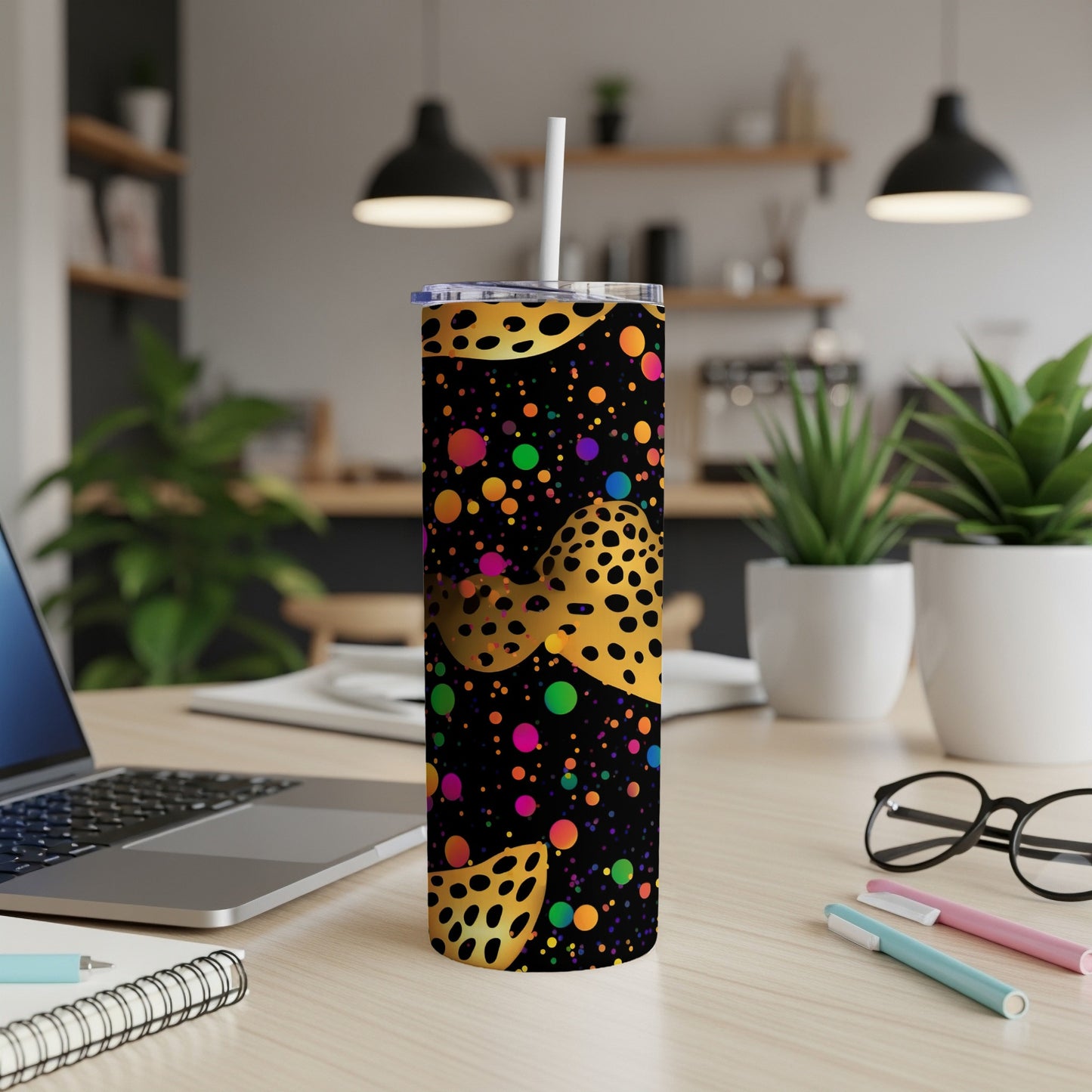 Black tumbler with colorful polka dots and yellow leopard spots, on a desk.