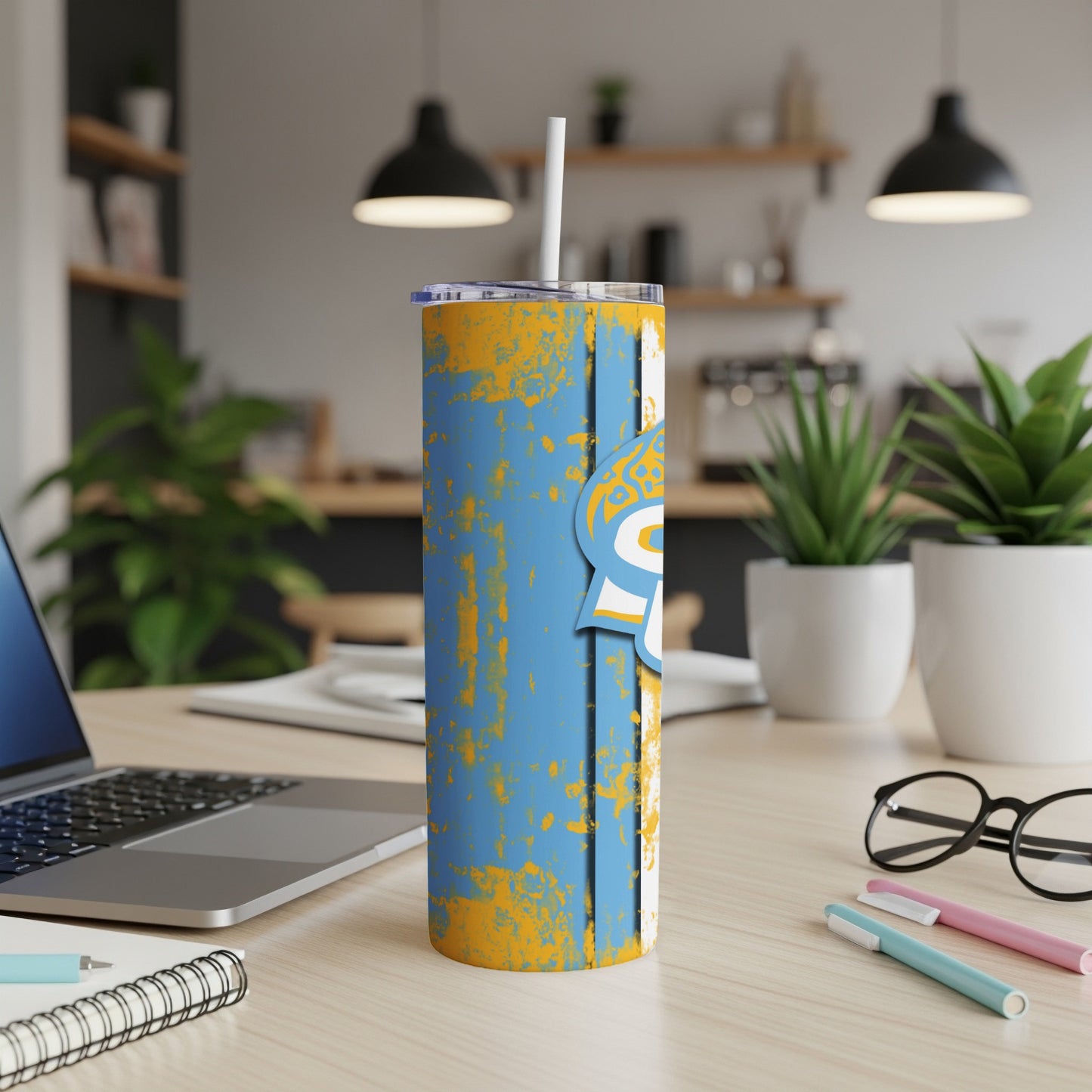 Blue and yellow distressed tumbler with straw on a wooden desk.