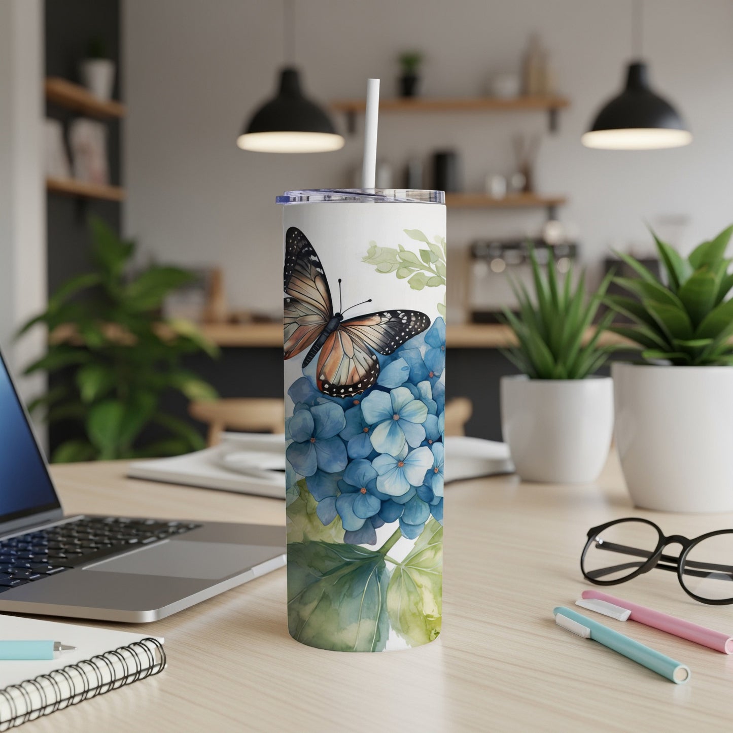 Tumbler with butterfly and blue hydrangeas on a desk.