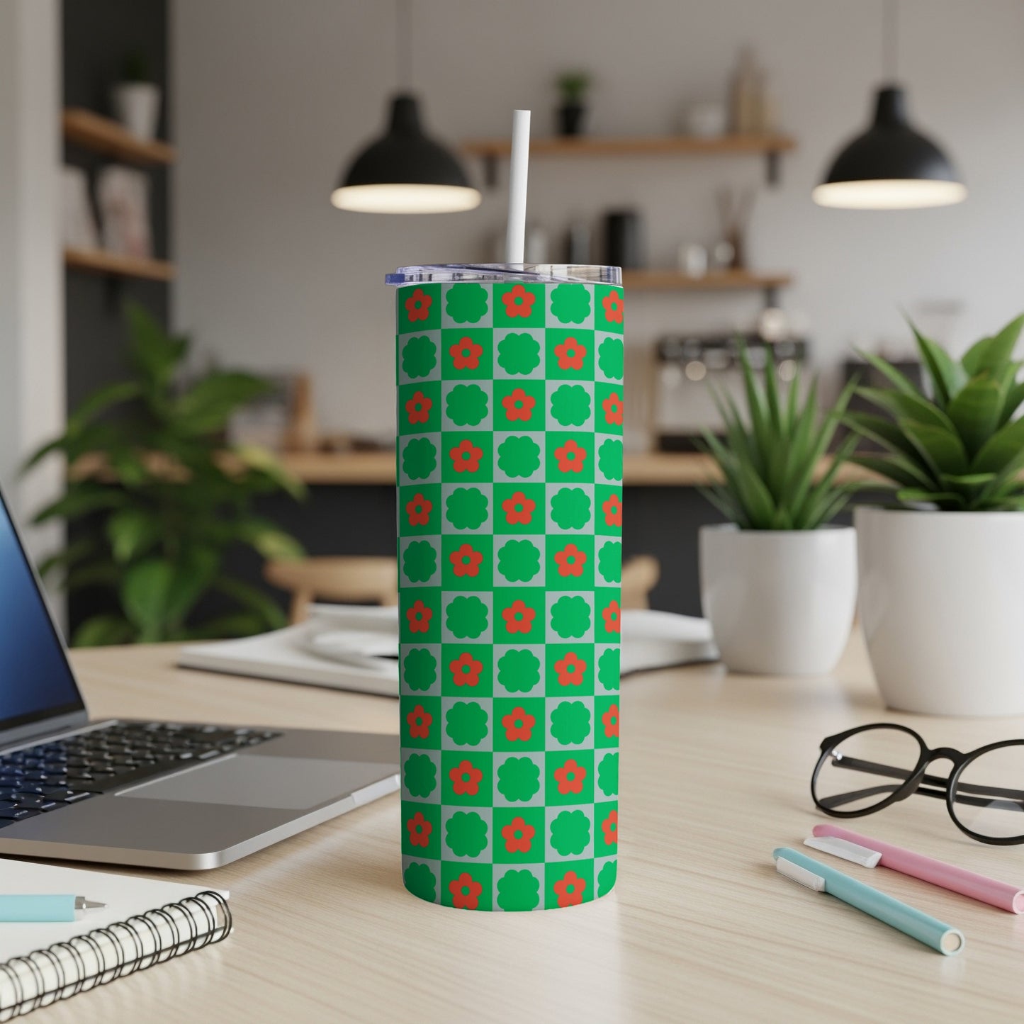 Green tumbler with red floral pattern, on desk with laptop and pens.