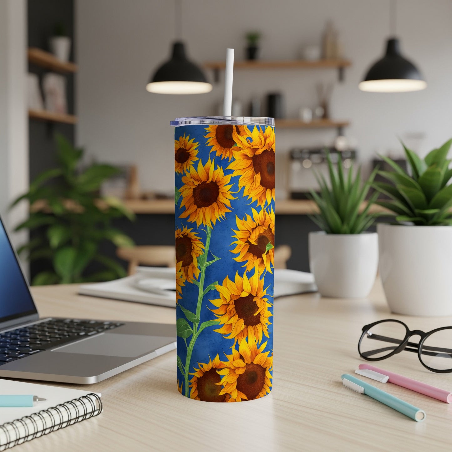 Blue tumbler with repeating sunflower pattern, on a desk with laptop.