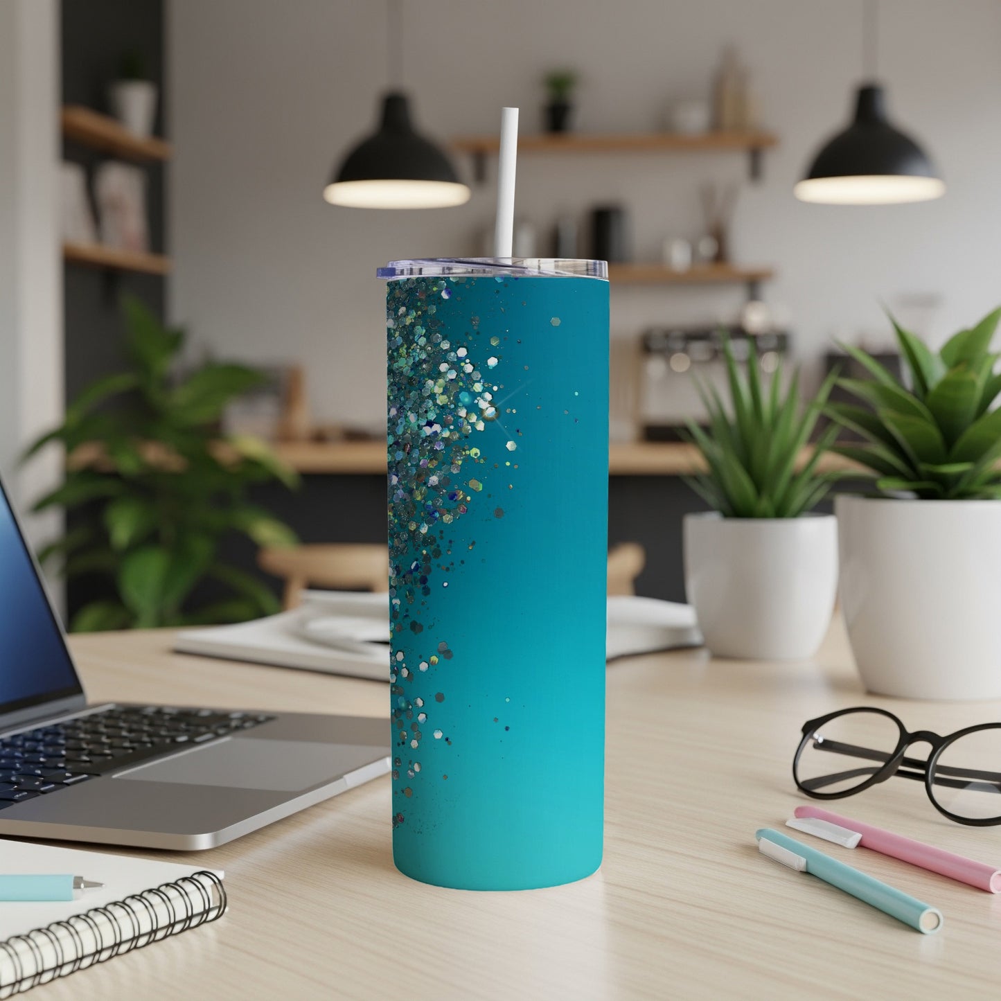 Teal glitter tumbler with a straw on a wooden desk.