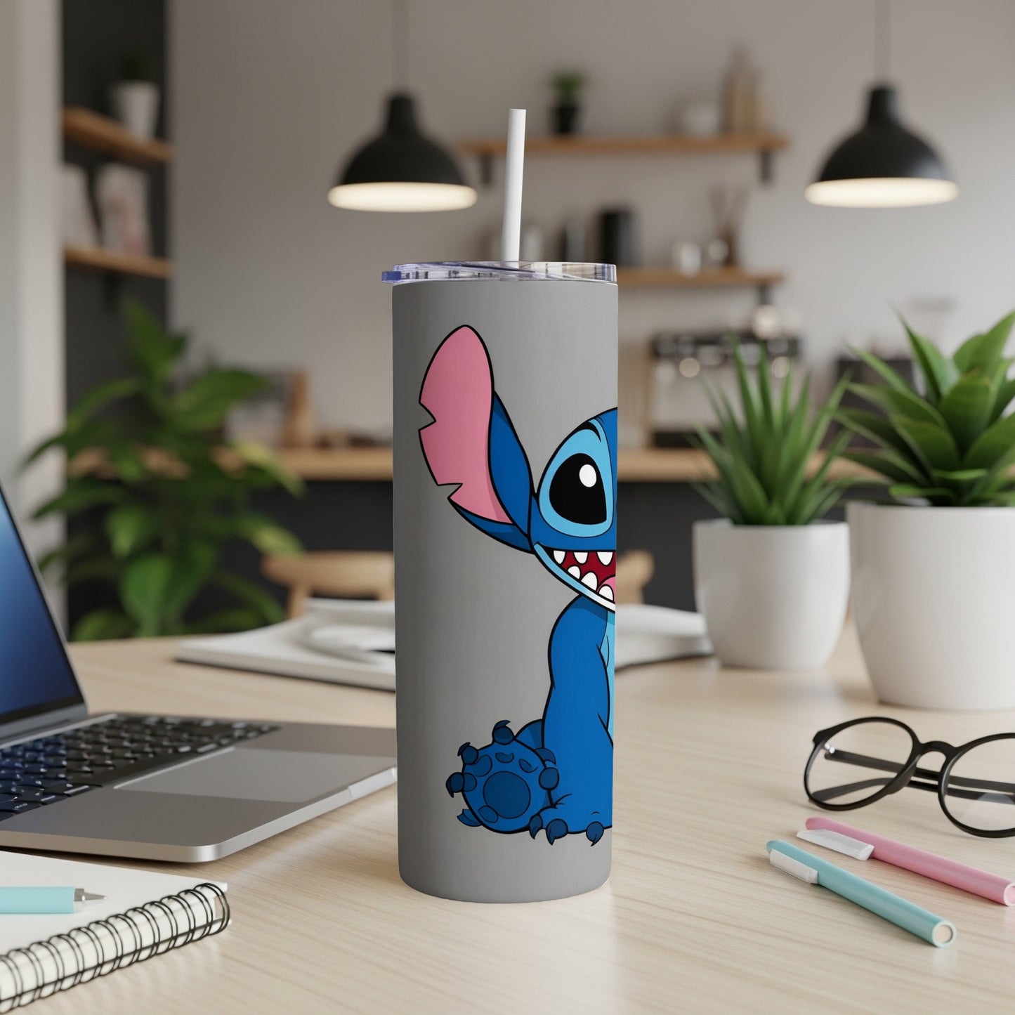 Stitch character on a grey tumbler with a straw on a desk.
