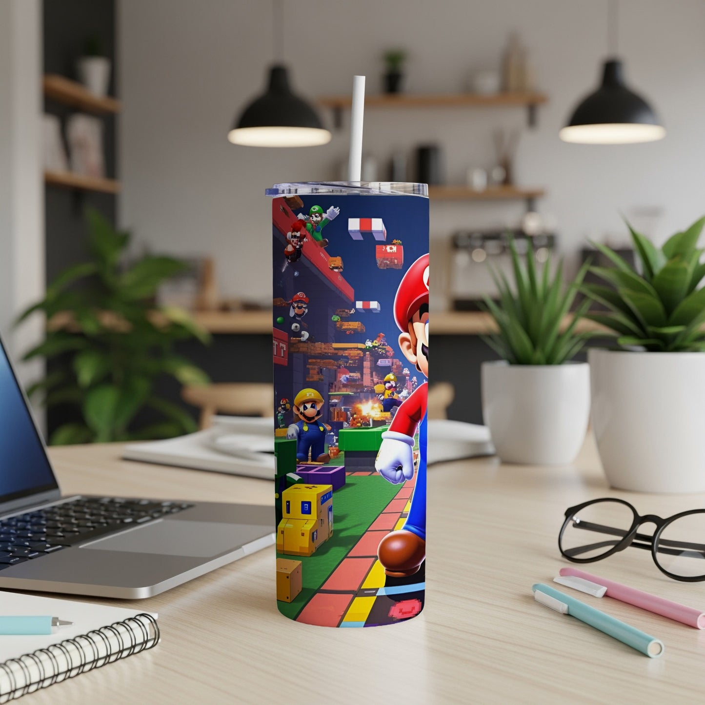Super Mario characters on a skinny tumbler next to a laptop and pens.