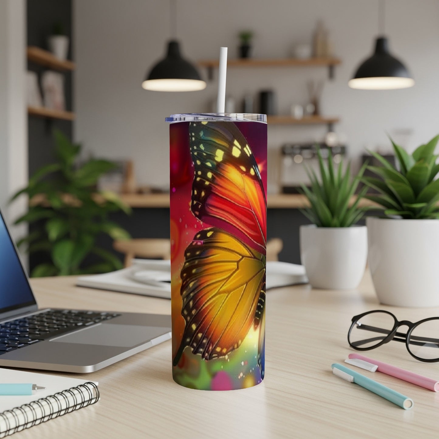 Tumbler with colorful butterfly design, on a desk with laptop and pens.