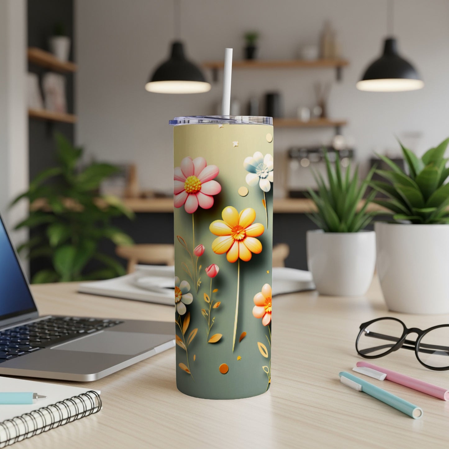 Tall tumbler with floral design and straw on a desk with a laptop.