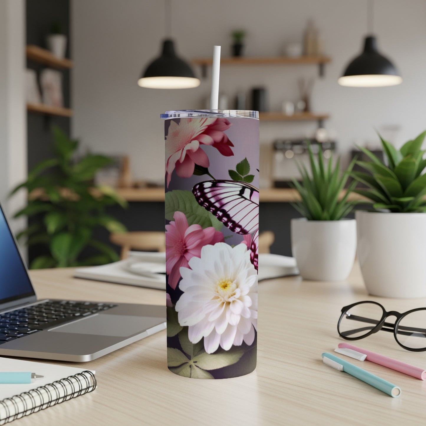 Floral butterfly tumbler with straw on a desk next to a laptop.