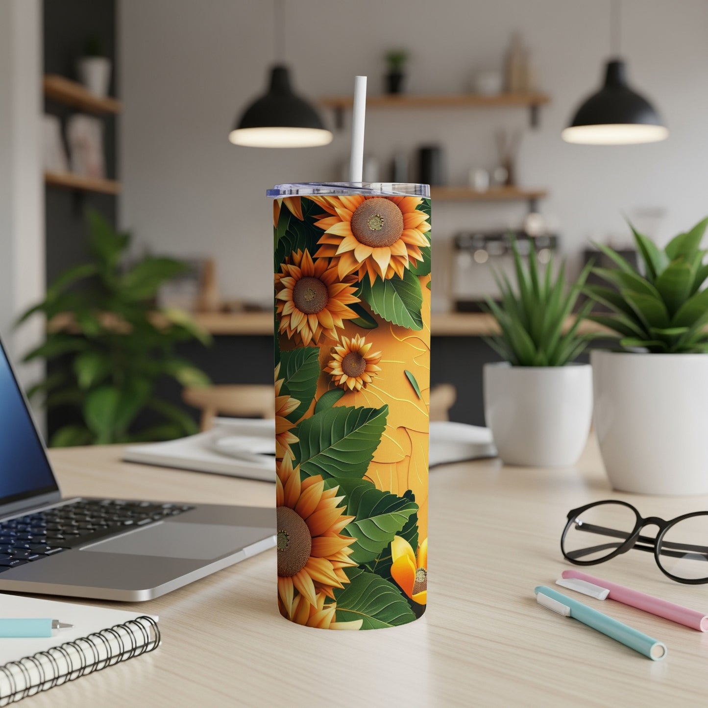 Tall tumbler with sunflower pattern and straw, on a desk.