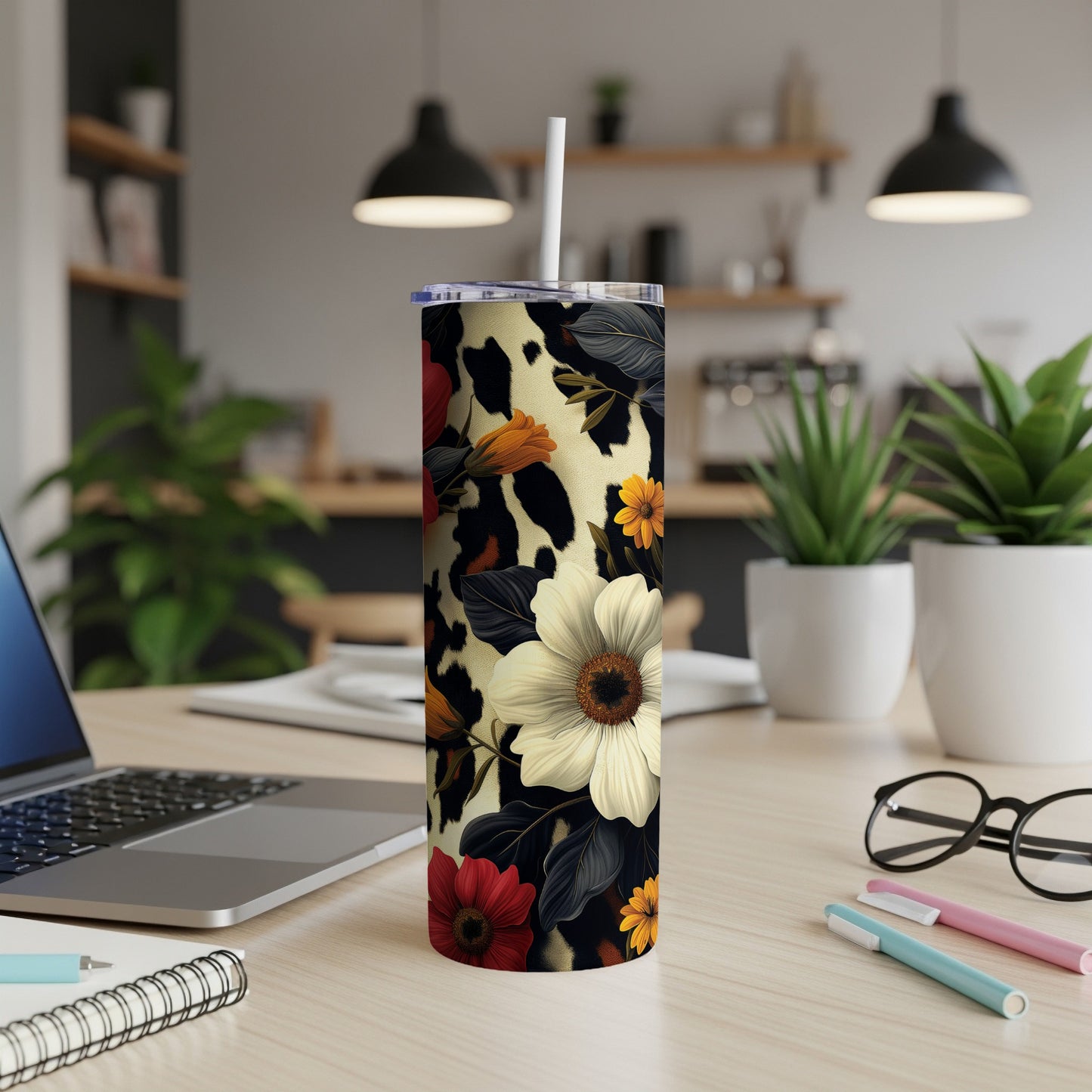 Tall tumbler with cow print and floral pattern, with a white lid and straw.