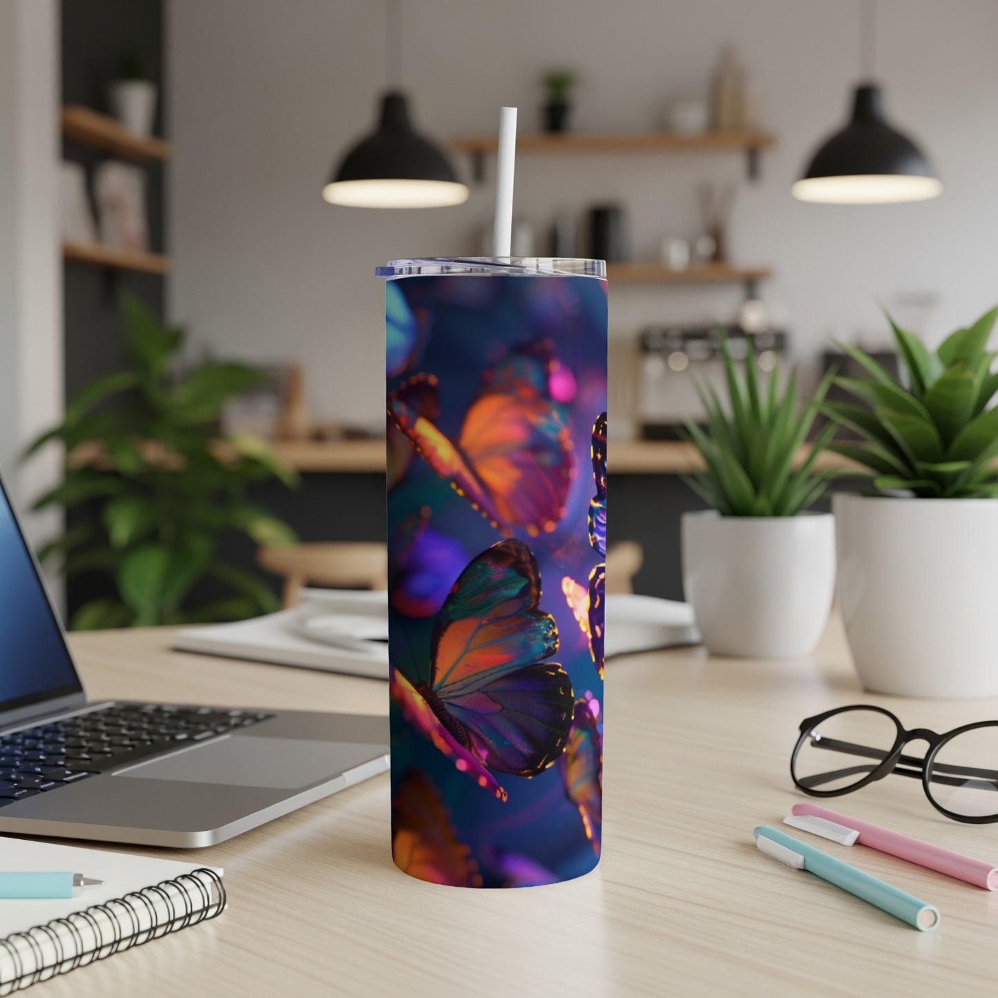 Tumbler with vibrant, glowing butterflies on a desk with a laptop and pens.