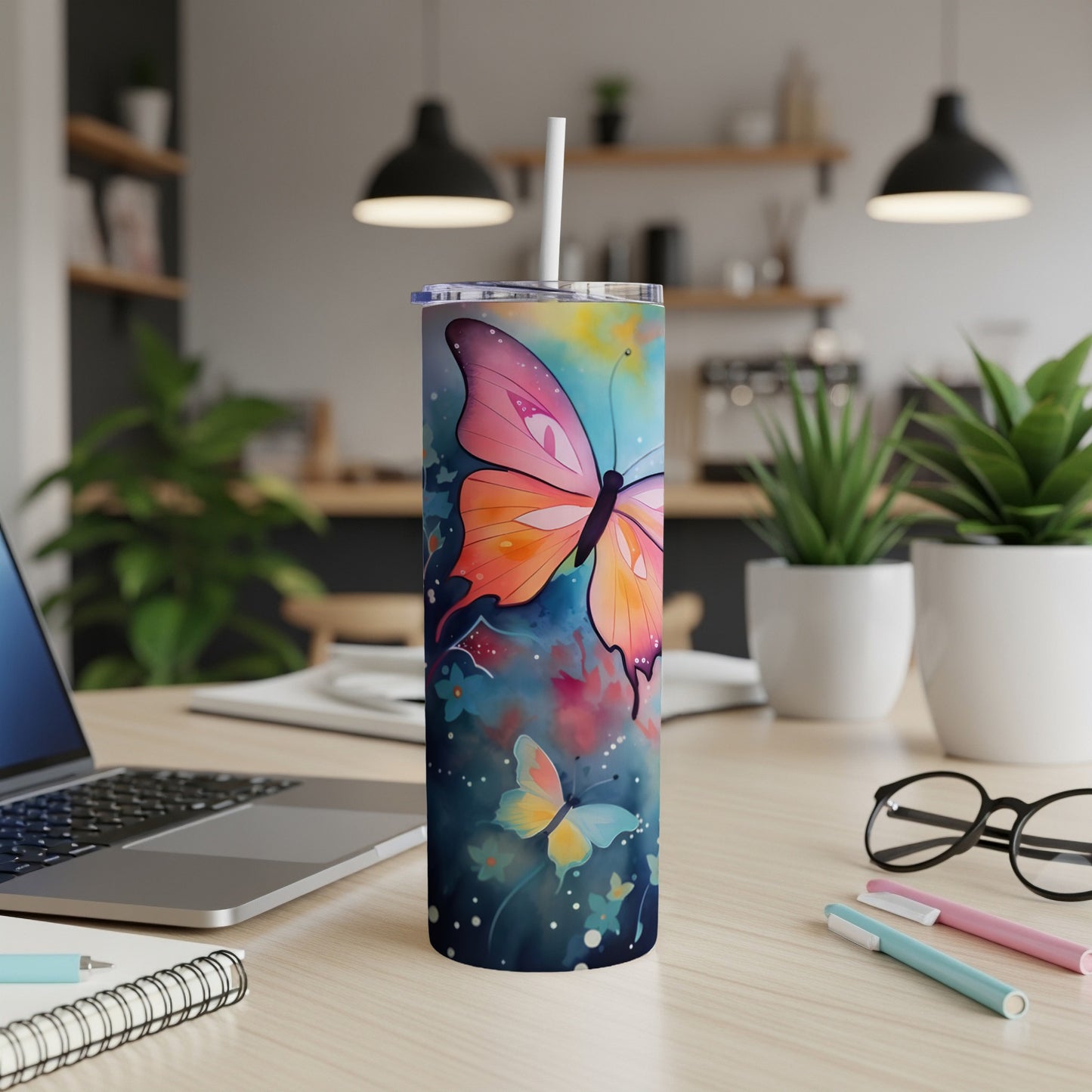 Butterfly-themed skinny tumbler with colorful design, straw, and writing supplies.