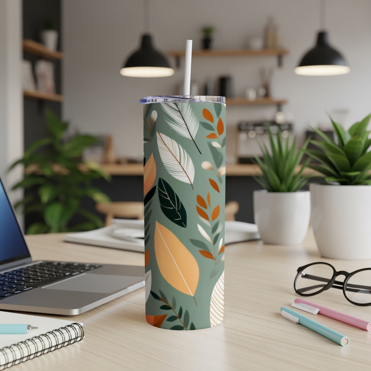 Green tumbler with a leaf pattern, featuring a straw, on a desk.