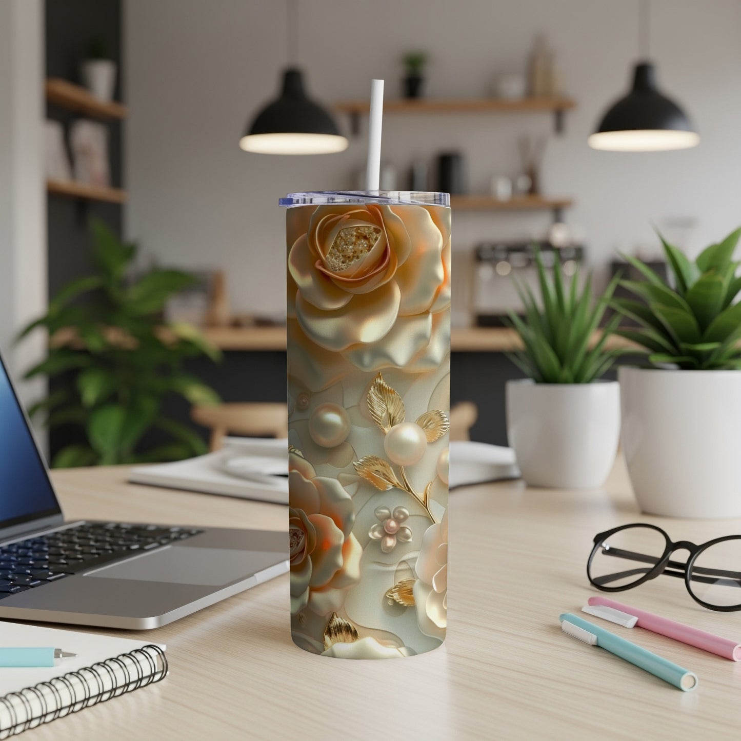 Gold floral patterned tumbler with straw on a desk.