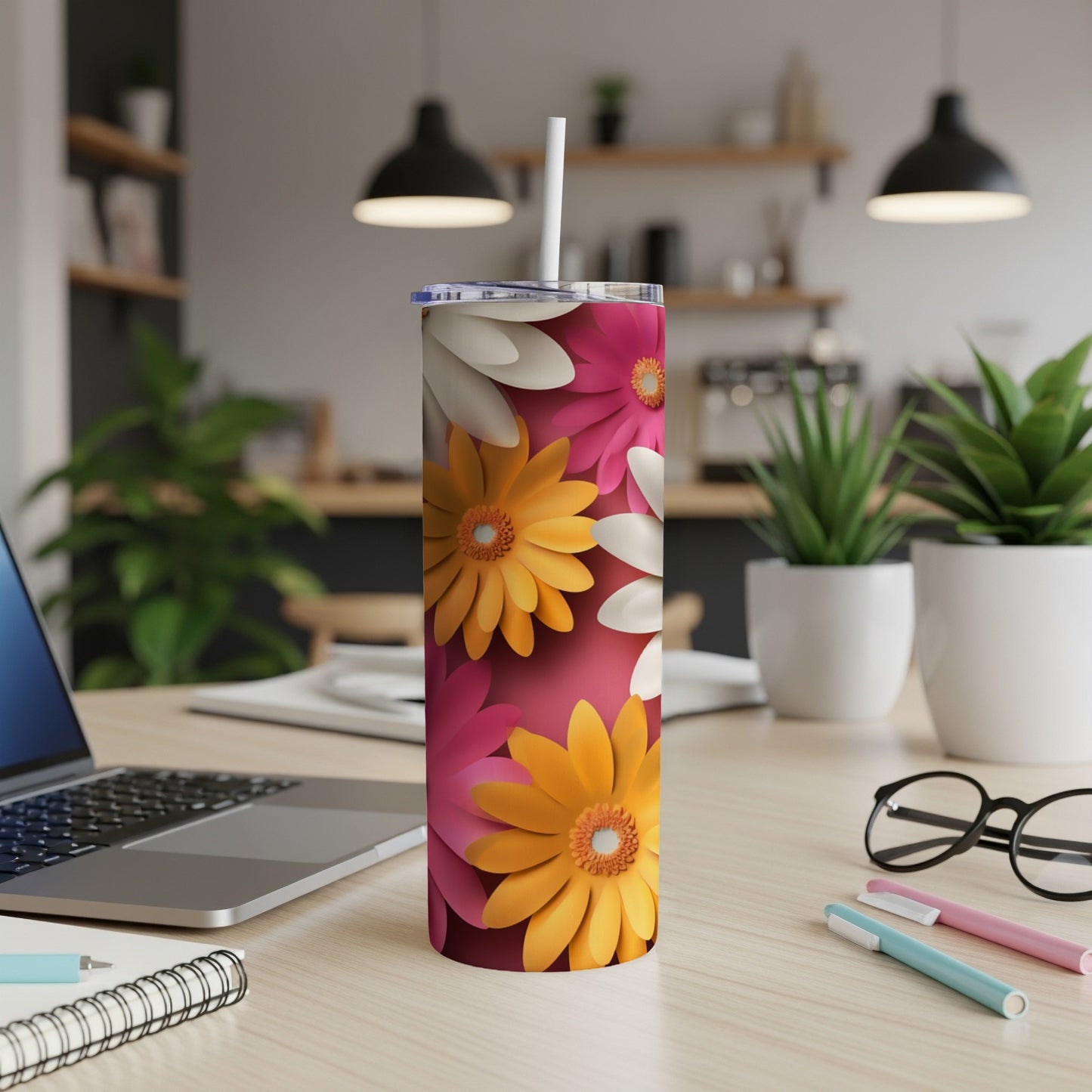 Pink and yellow floral tumbler with straw on a desk.