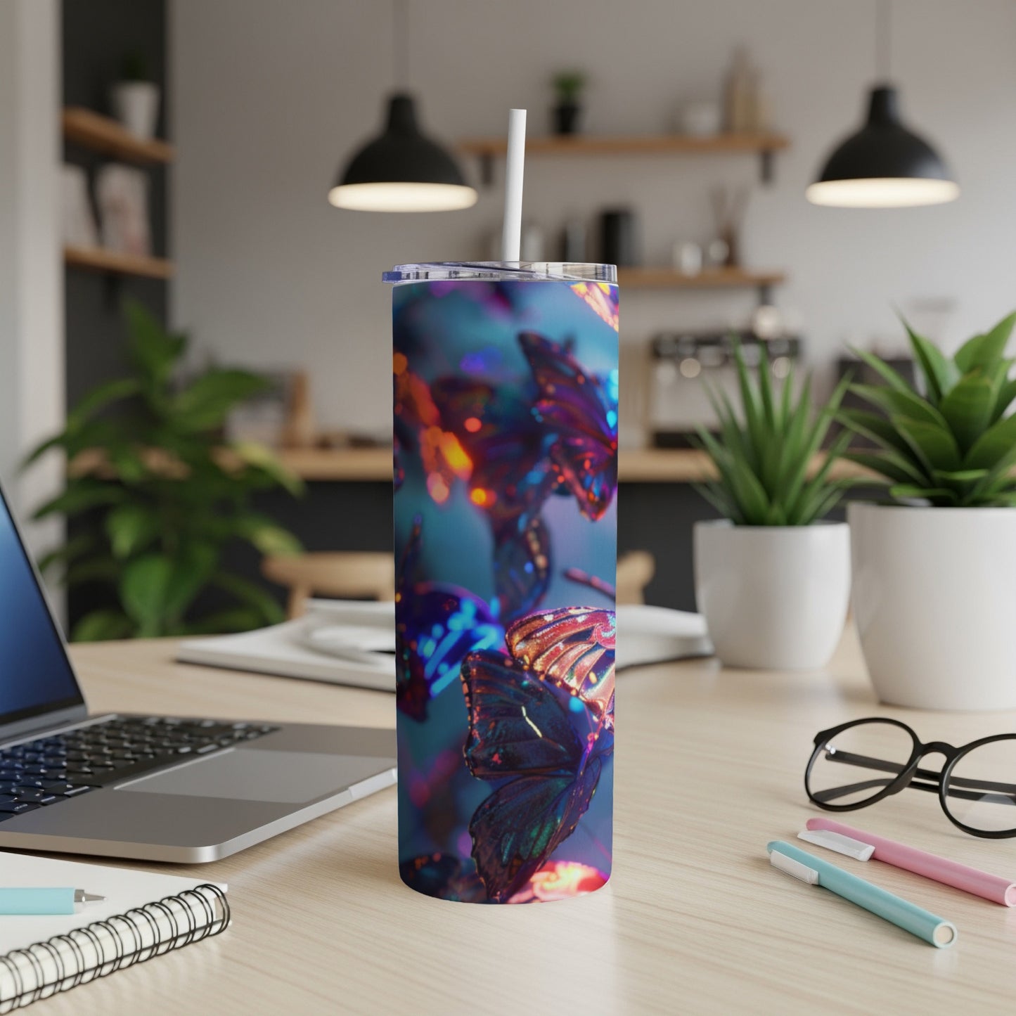 Tumbler with iridescent butterfly pattern on a desk with a laptop and pens.