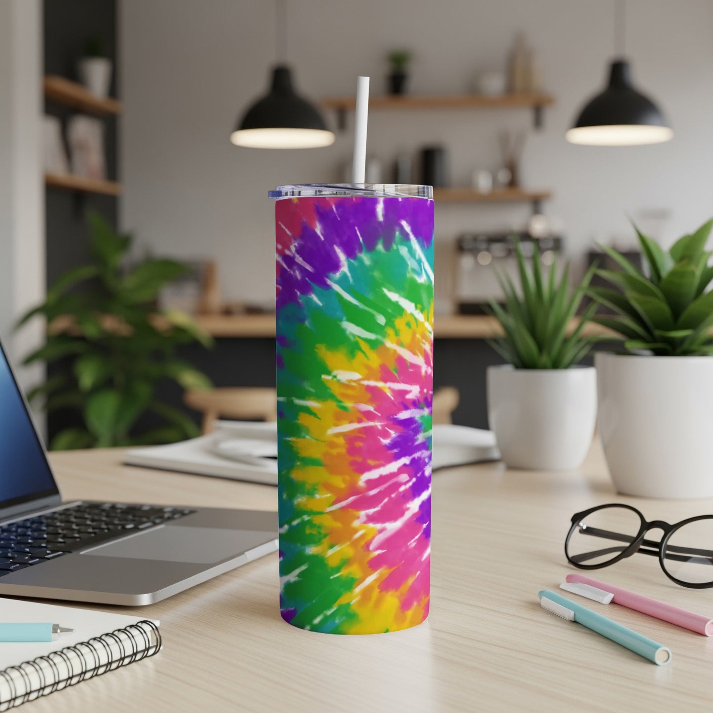 Tie-dye tumbler with straw on a desk next to a laptop and pens.