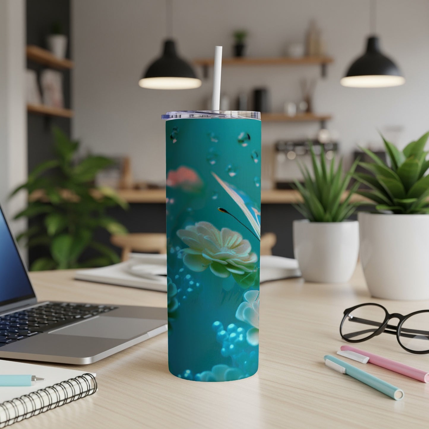 Teal tumbler with a floral and butterfly design, on a desk.
