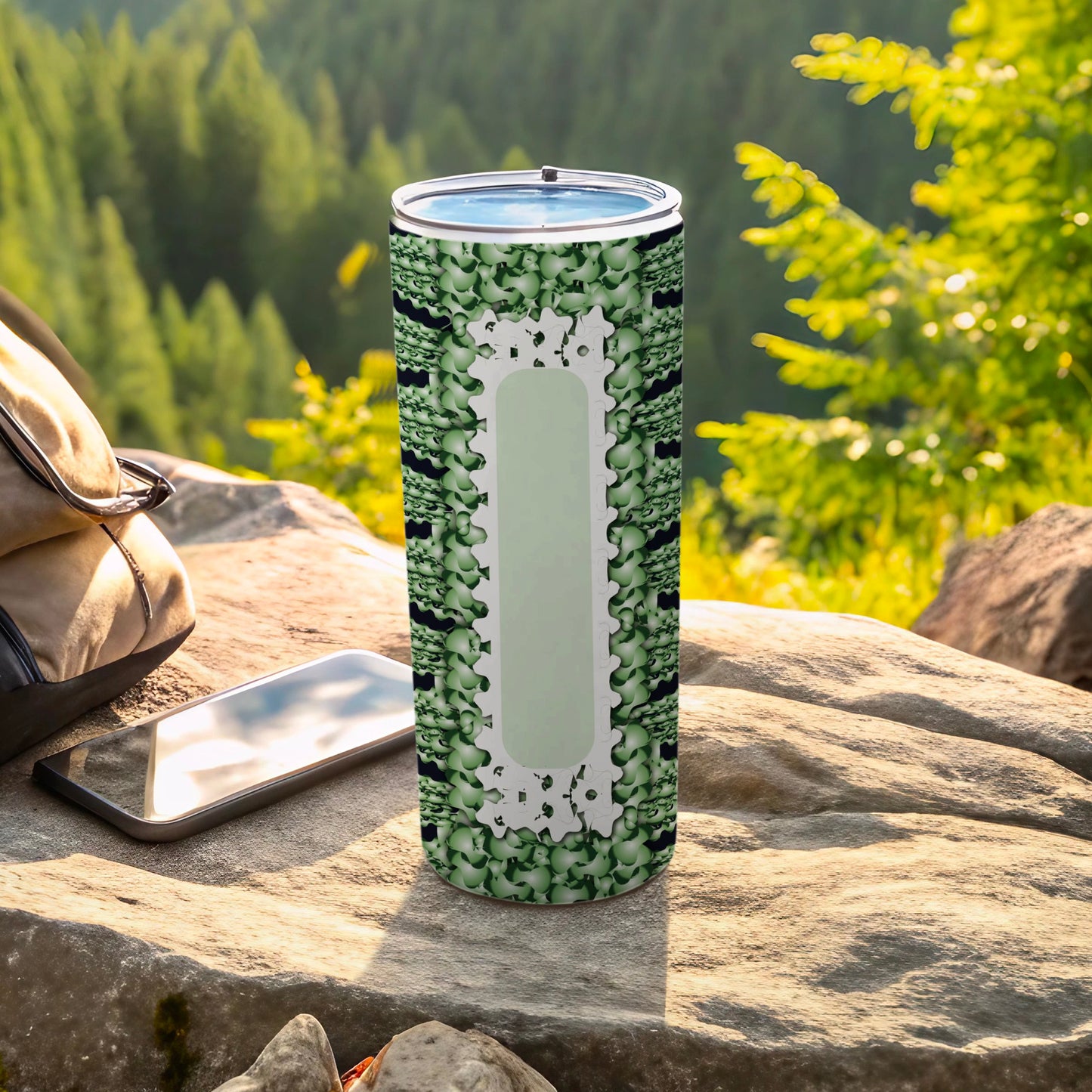 Green patterned tumbler resting on rocks with a backpack and phone.
