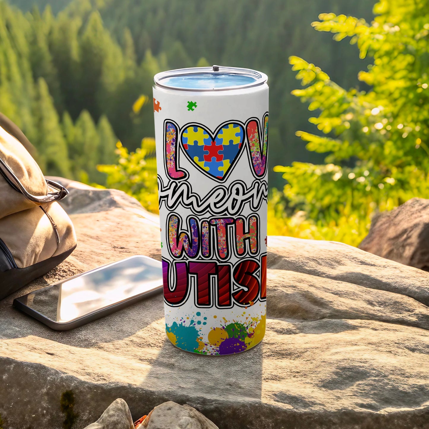 Tumbler with "Love Someone With Autism" puzzle design and colorful paint splatters.