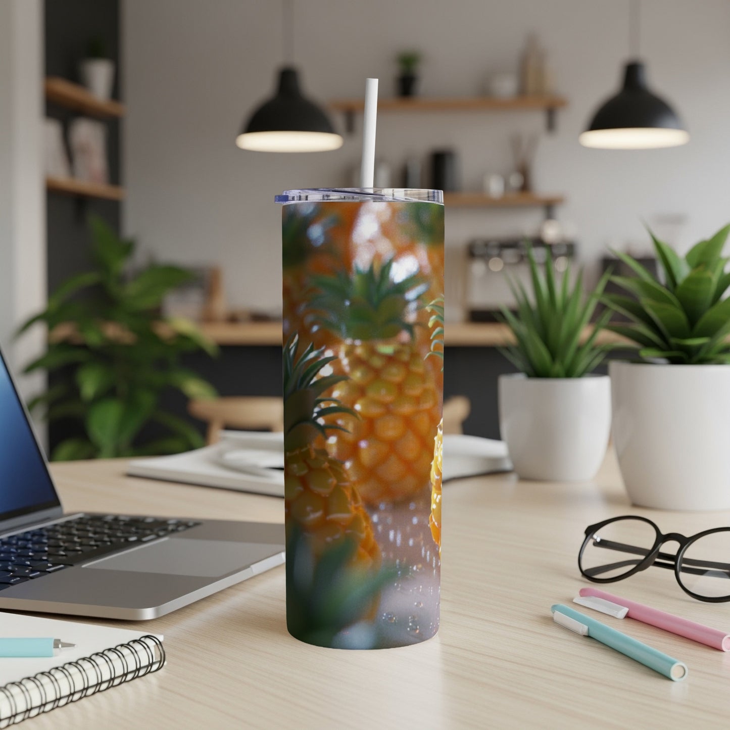 Pineapple pattern tumbler with straw on a desk next to a laptop.