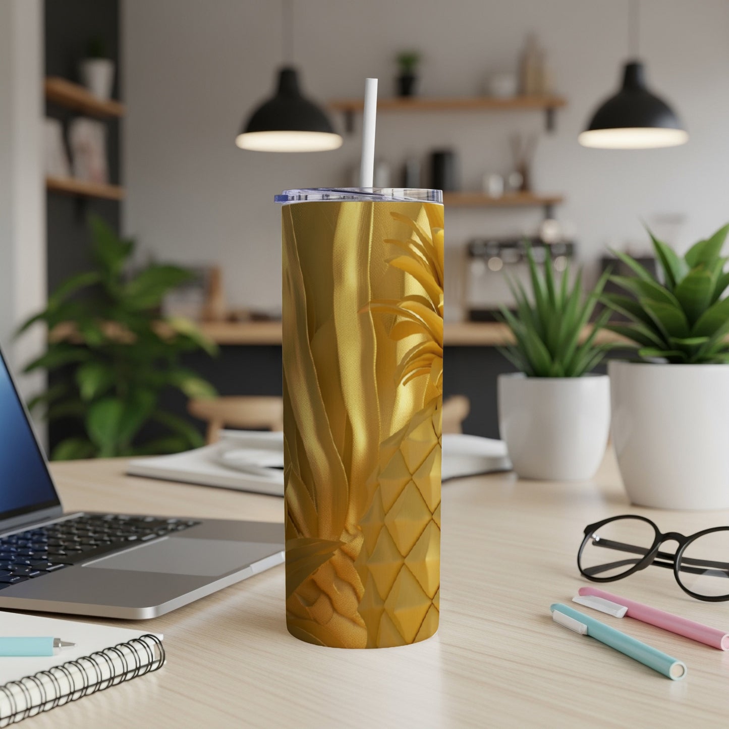 Gold pineapple tumbler with straw on a desk next to a laptop.