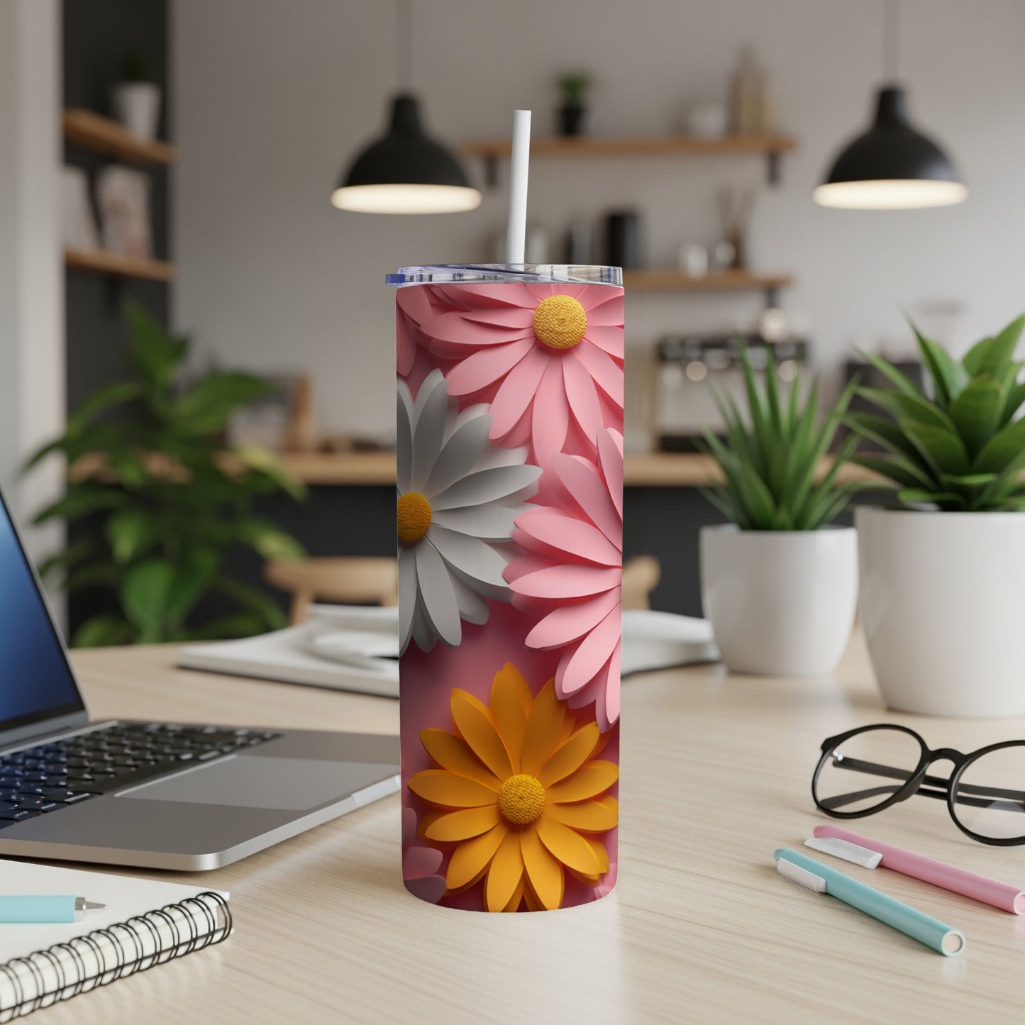 Pink, white, and yellow daisy pattern on a pink tumbler with straw on a desk.