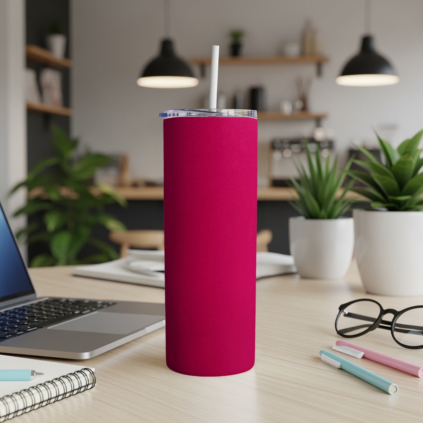 Plain pink tumbler with white straw on desk next to laptop.